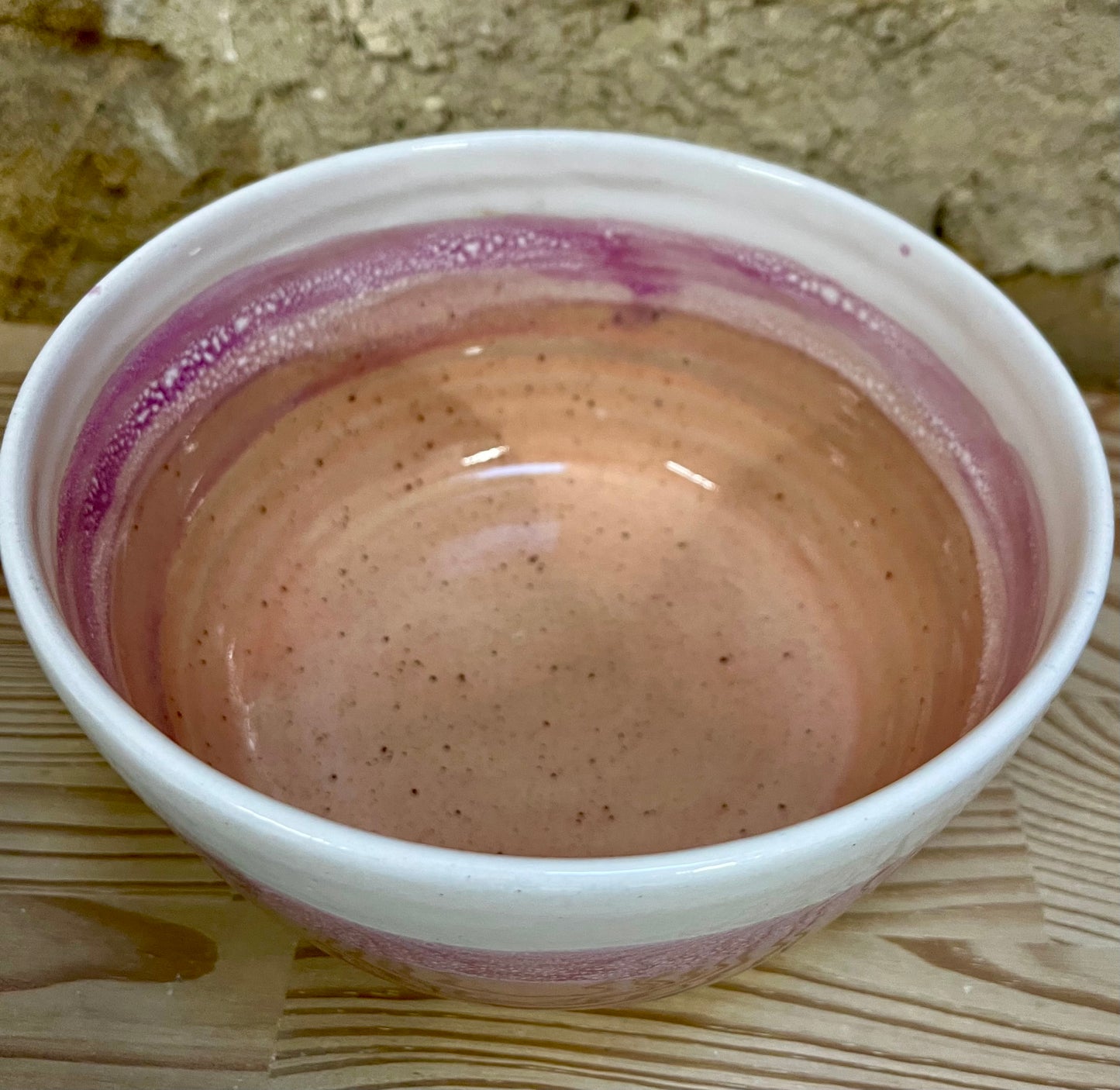 pink, orange and white bowl on a wooden surface with a stone wall background