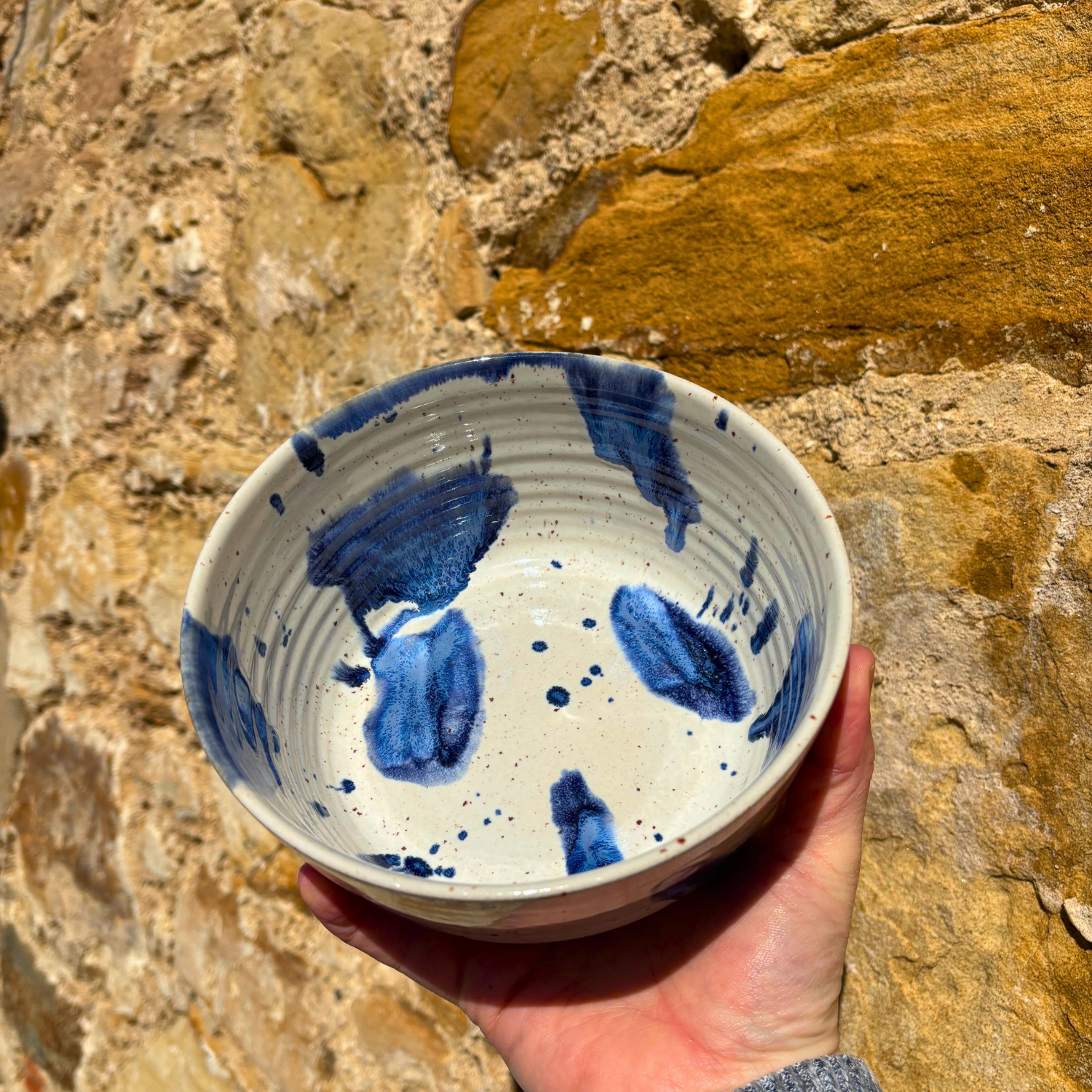 Hand holding a ceramic bowl with blue abstract designs against a stone wall background