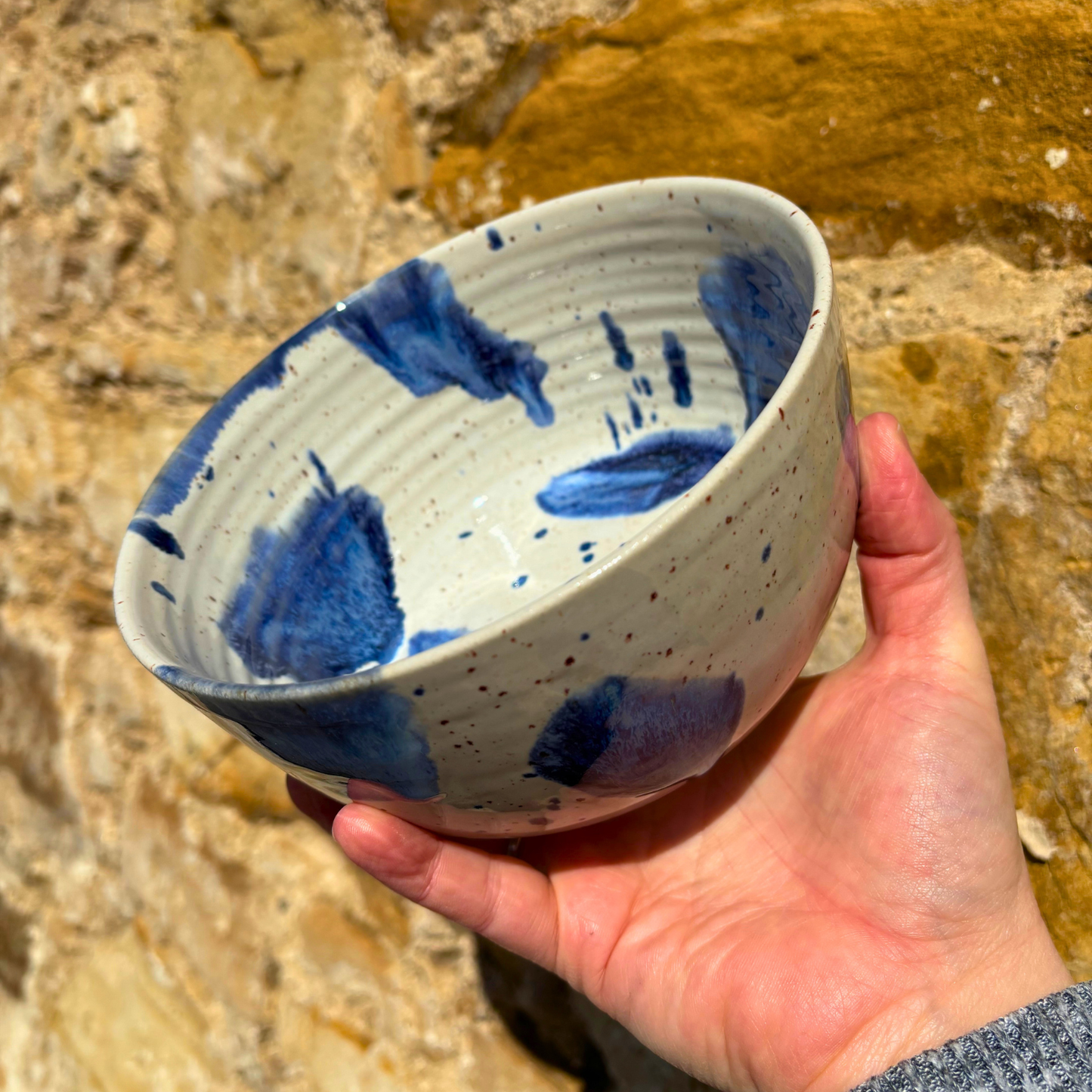 Hand holding a ceramic bowl with blue abstract patterns against a natural stone background