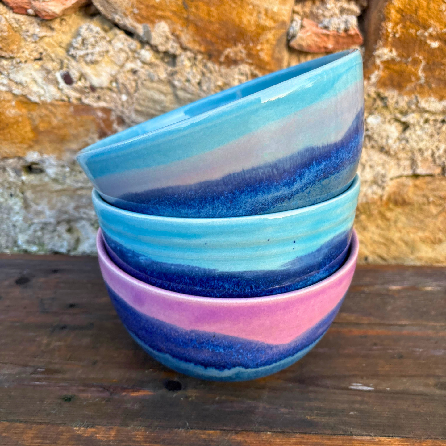 Stack of colorful ceramic bowls against a stone wall.