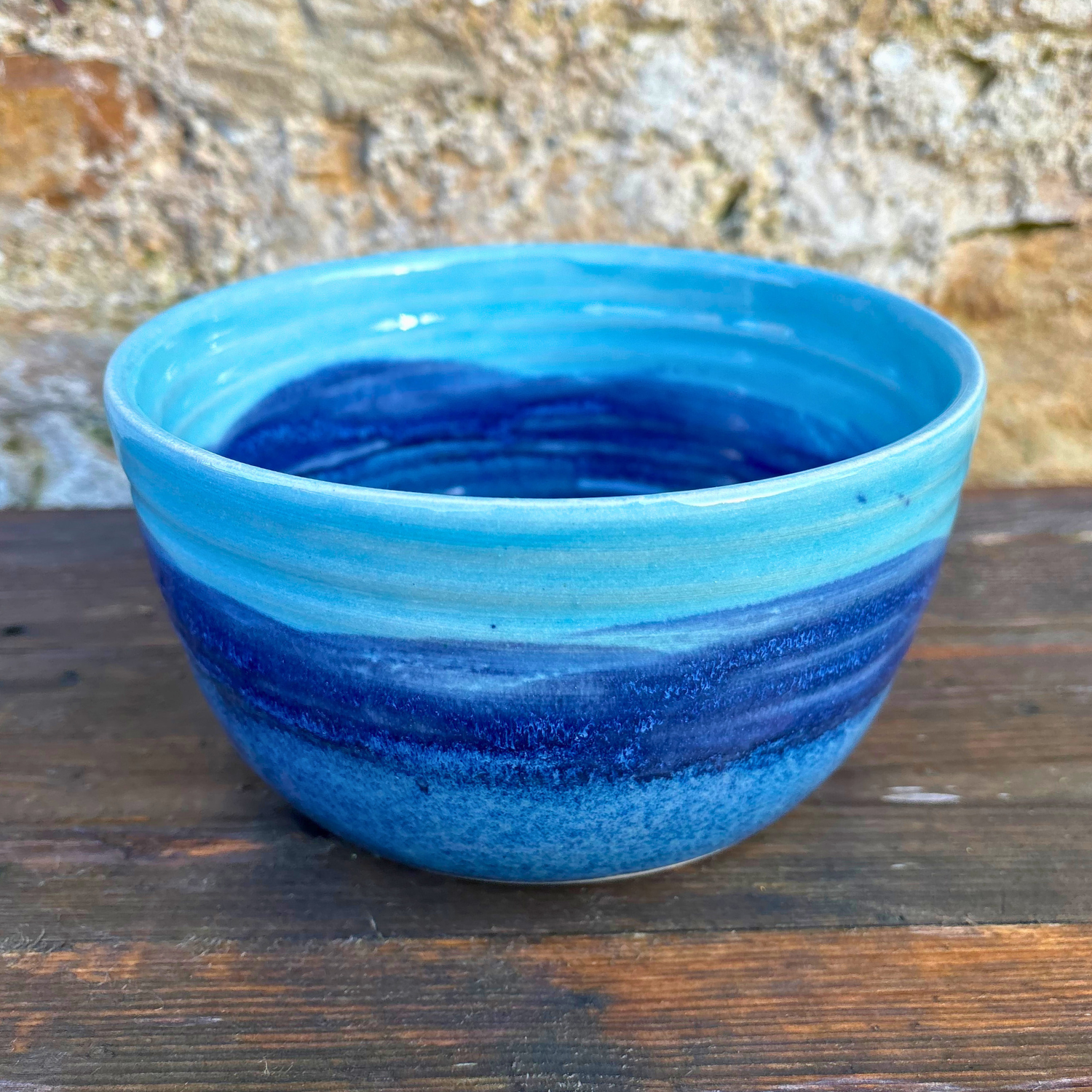Blue ceramic bowl on a wooden surface with a stone wall background