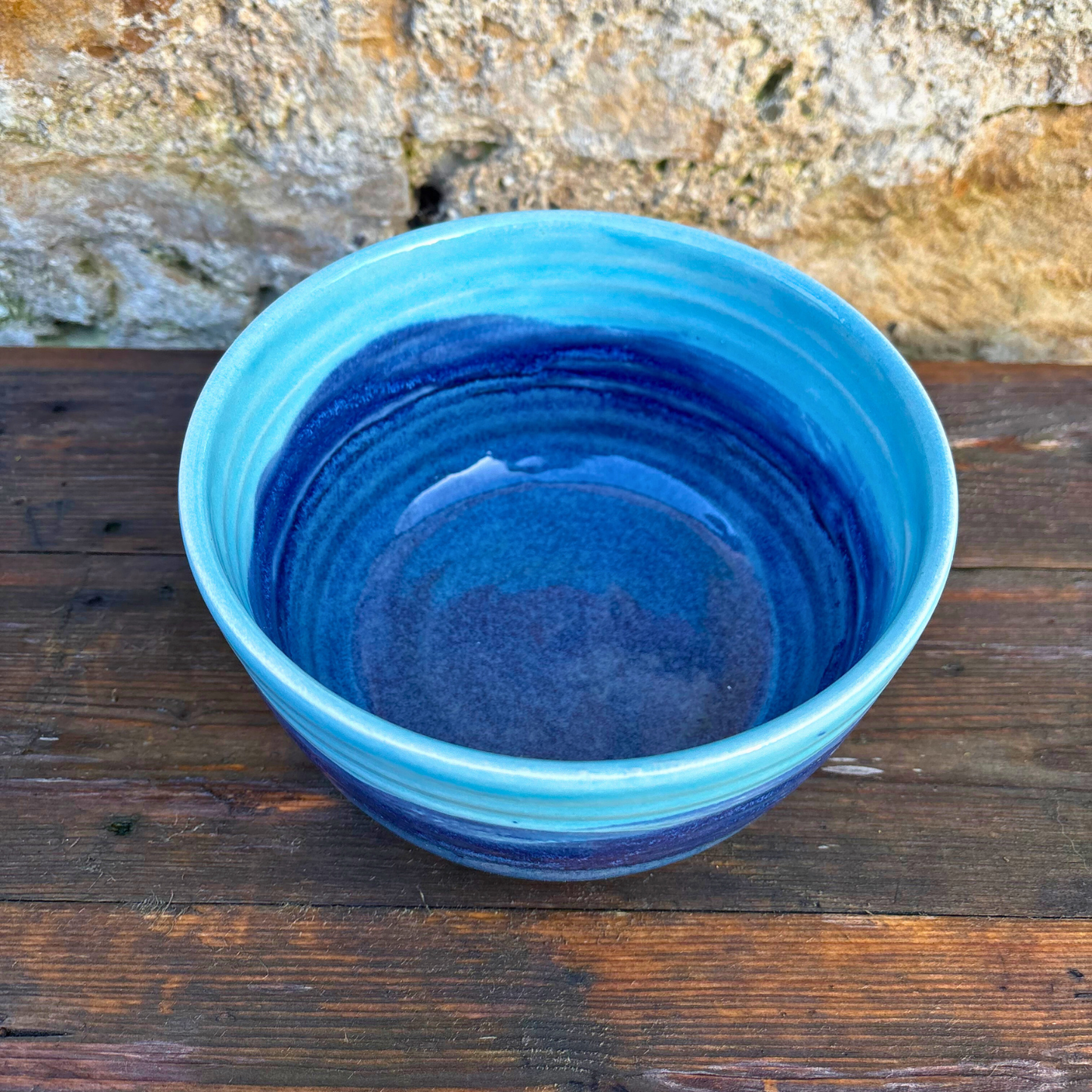Blue ceramic bowl on a wooden surface with a stone wall background