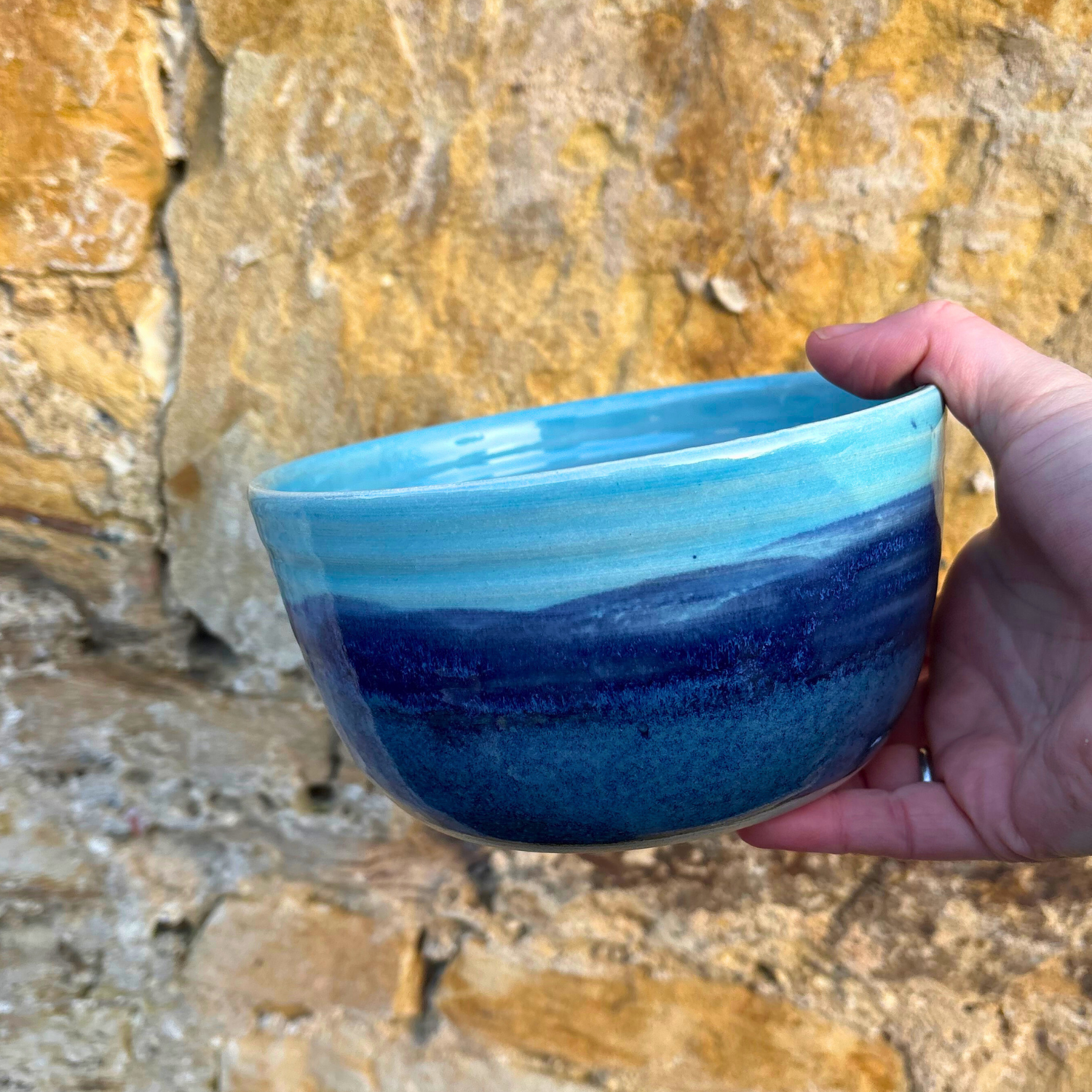 Hand holding a blue ceramic bowl against a stone wall background
