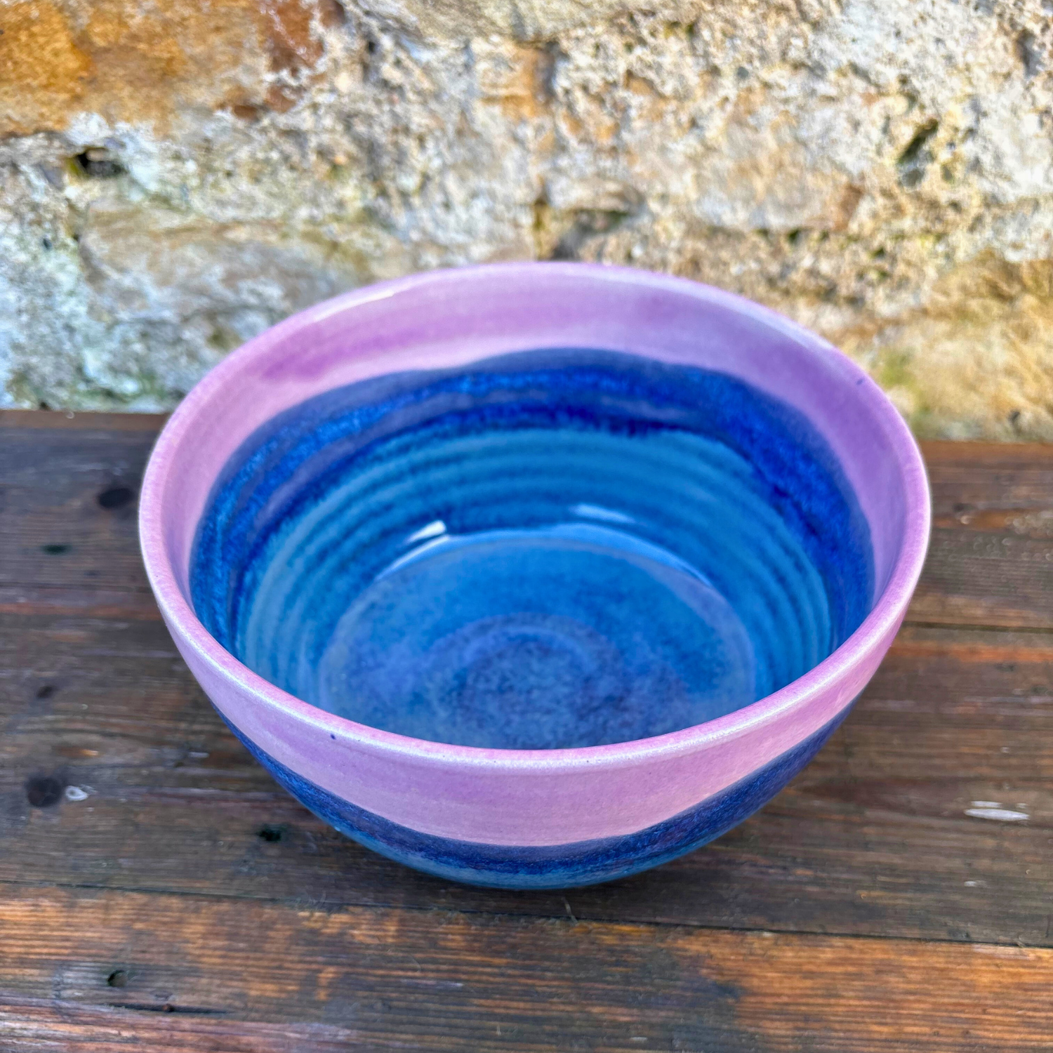 Pink and blue ceramic bowl on a wooden surface with a stone wall background