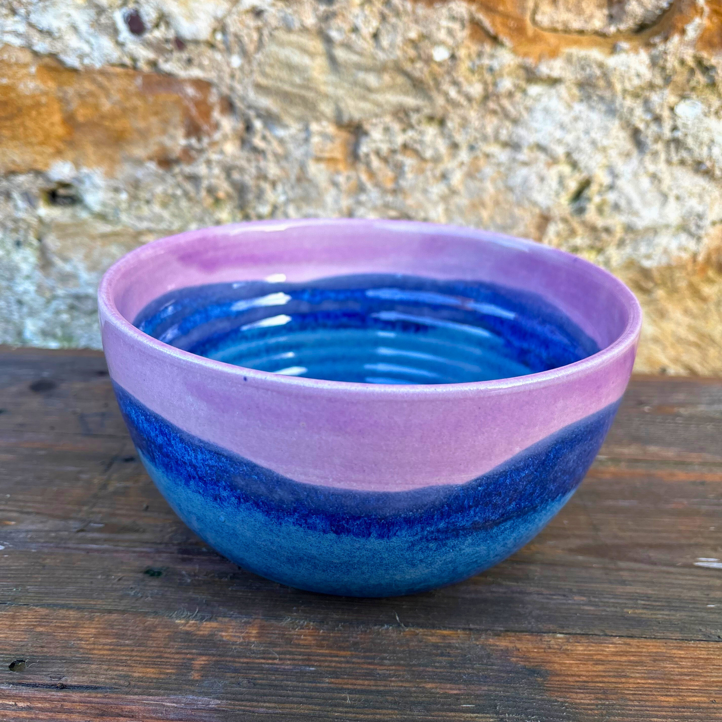 Ceramic bowl with blue and purple glaze on a wooden surface with a stone wall background