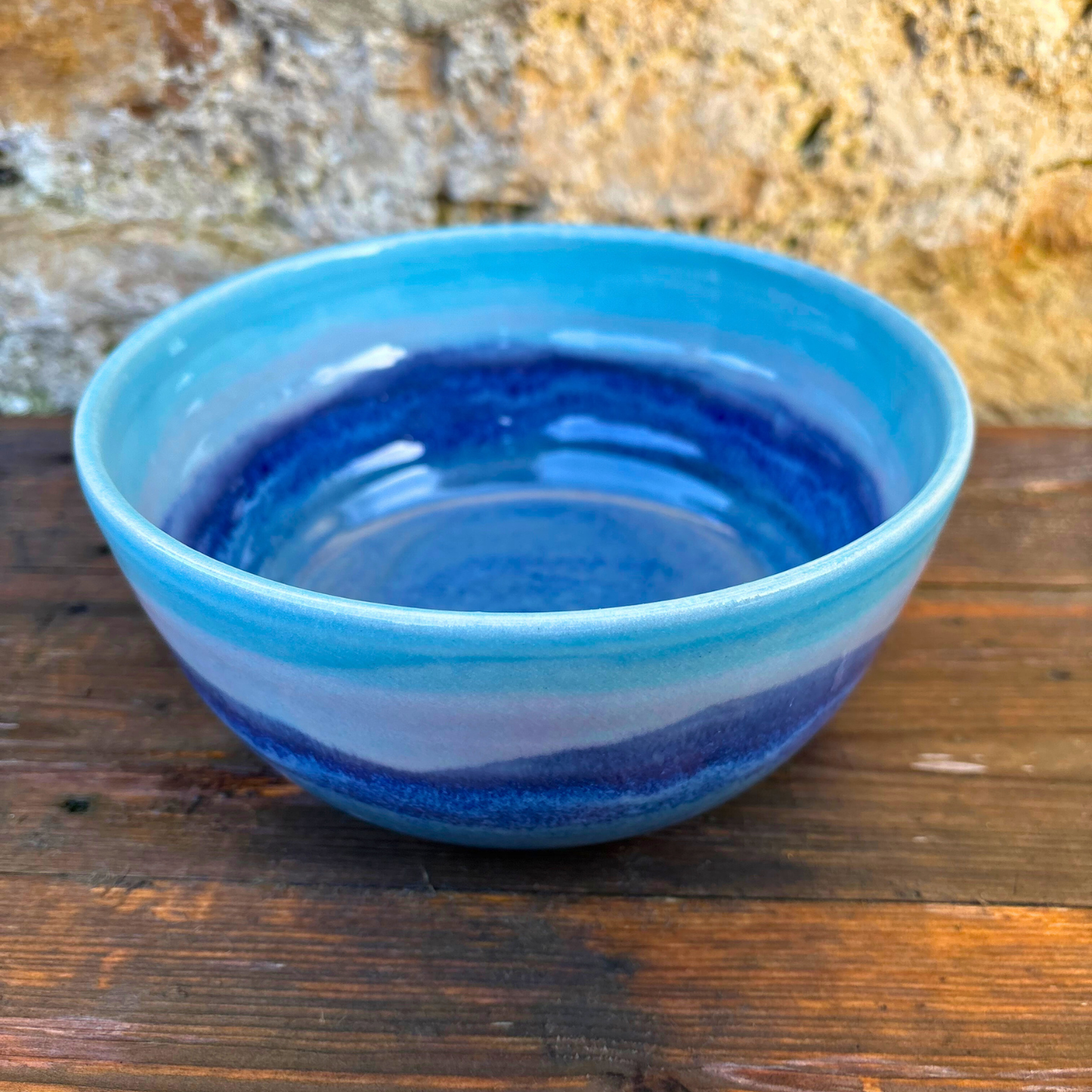 Blue ceramic bowl on a wooden surface with a stone wall background