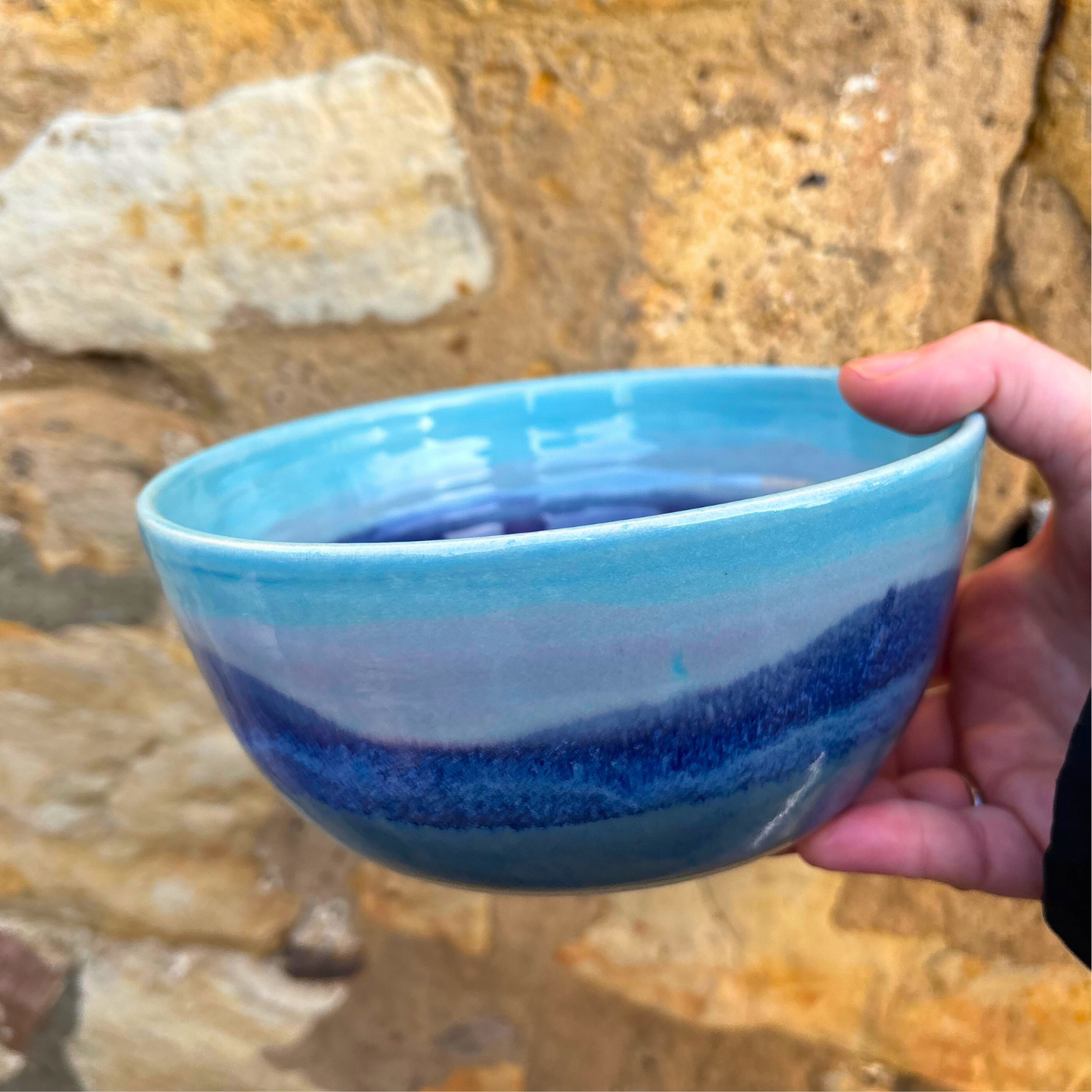 Hand holding a blue ceramic bowl against a natural stone background