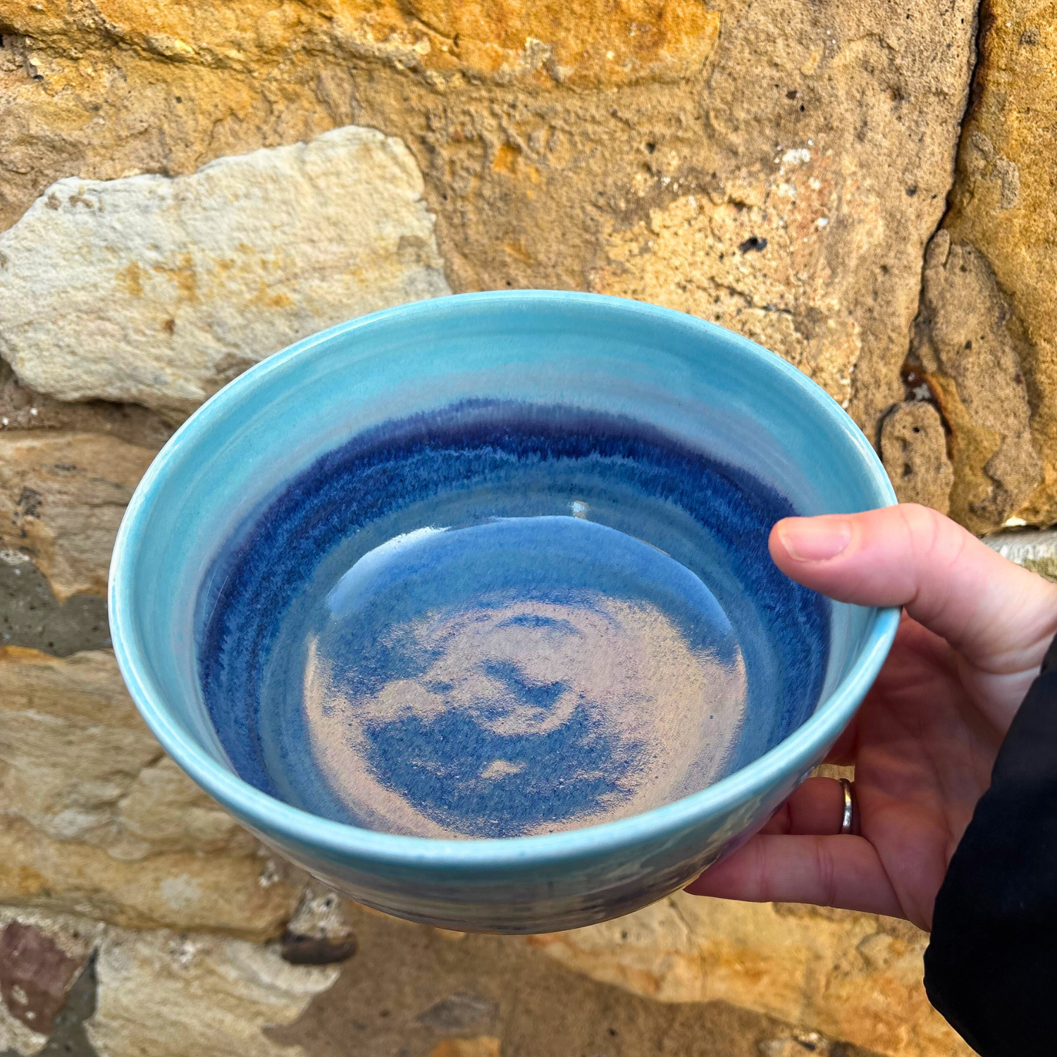 Blue ceramic bowl held by a hand against a stone background