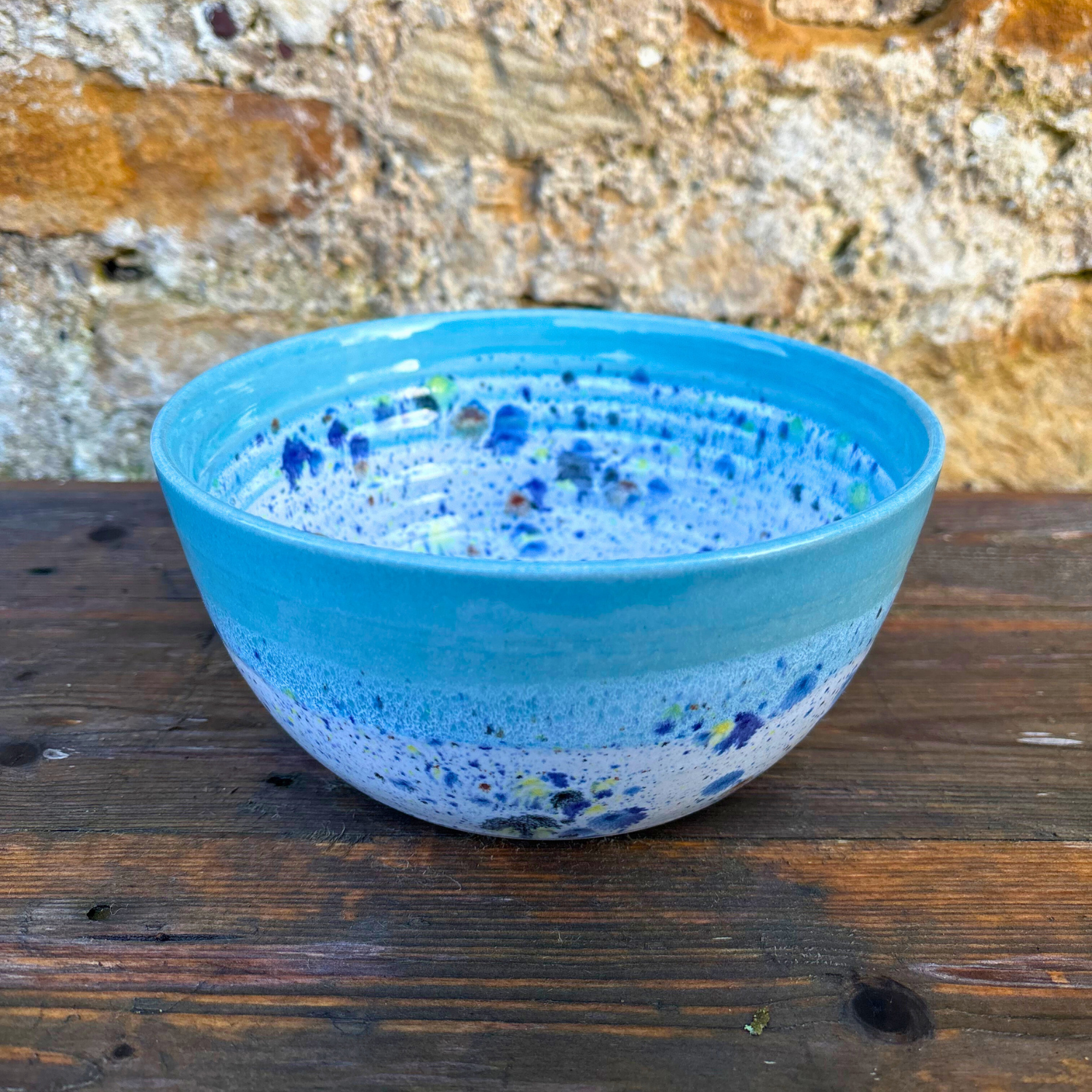 Blue ceramic bowl with speckled pattern on a wooden surface with a stone wall background