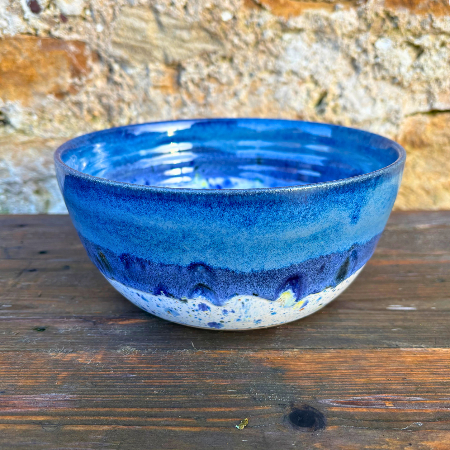 Blue ceramic bowl on a wooden surface with a stone wall background
