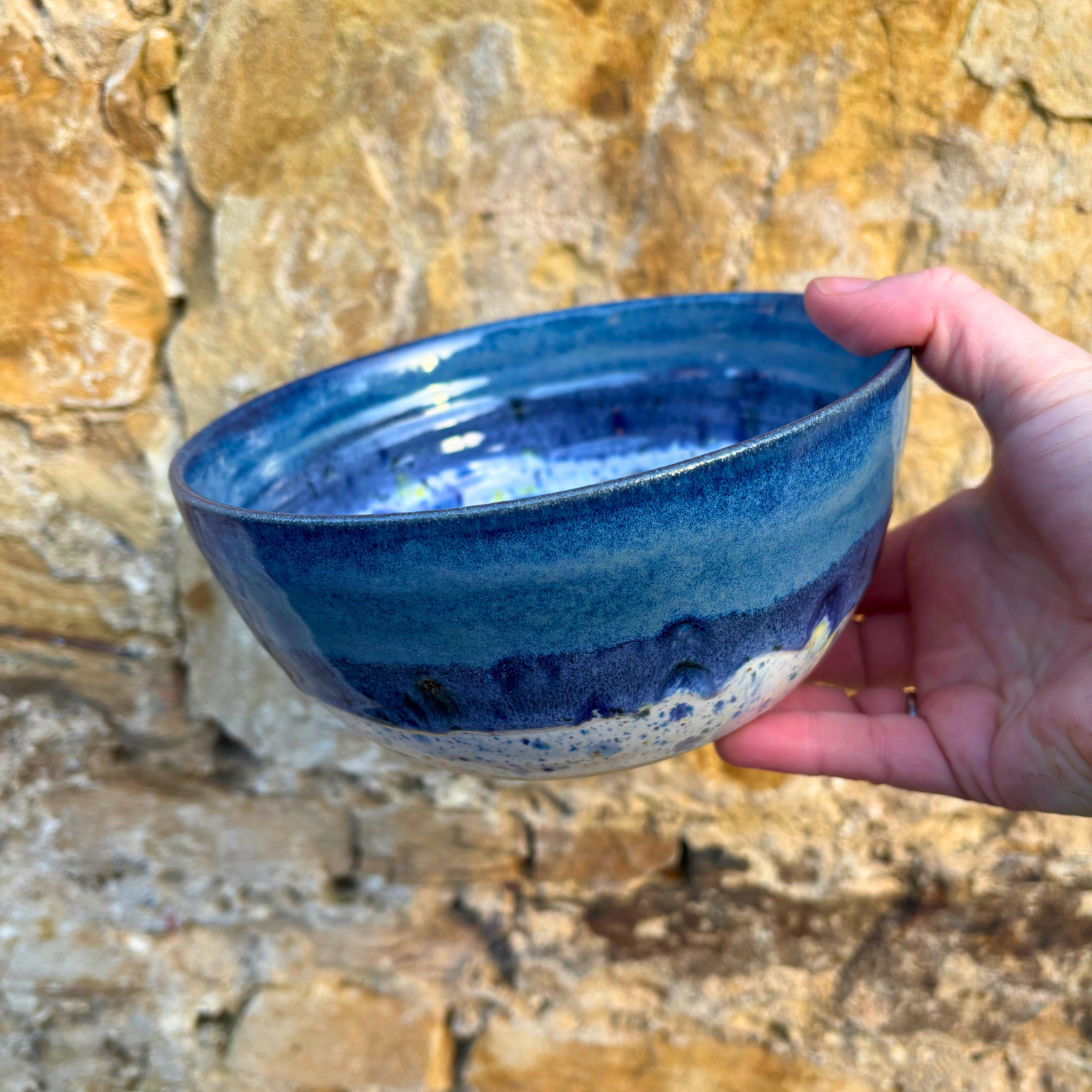 Hand holding a blue ceramic bowl against a stone wall background