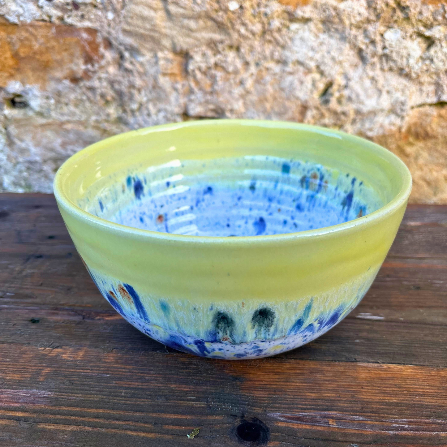 Yellow ceramic bowl with blue speckles on a wooden surface