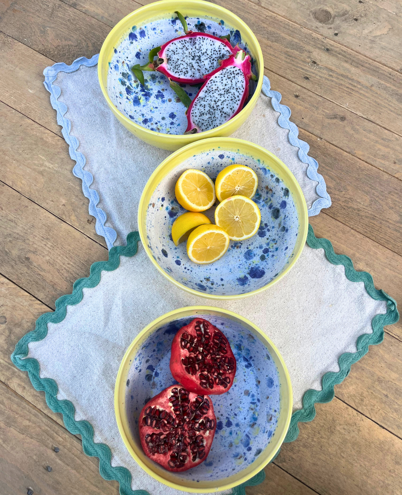 Three ceramic bowls with dragon fruit, lemons, and pomegranate on a wooden surface.