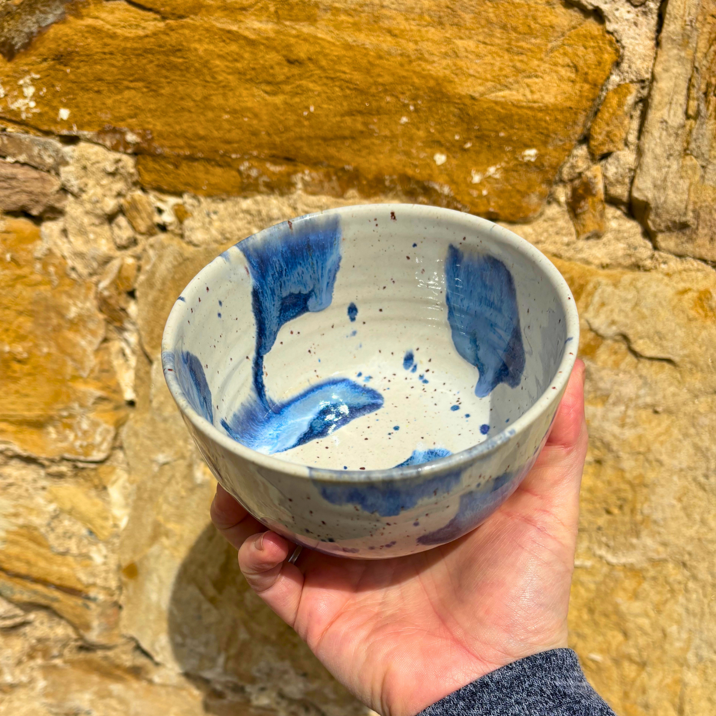 Hand holding a ceramic bowl with blue abstract patterns against a stone background
