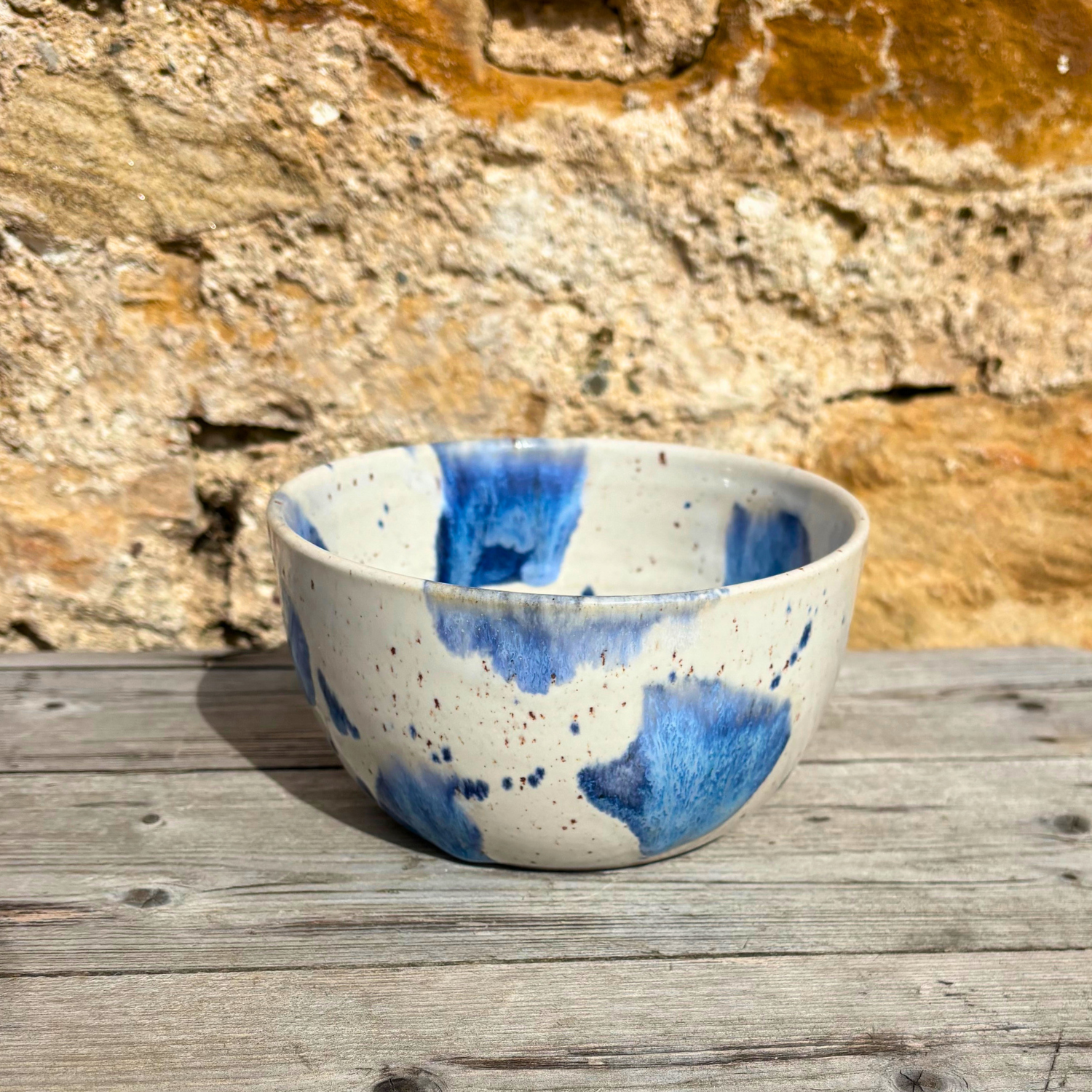 Ceramic bowl with blue speckled design on a wooden surface with a stone wall background