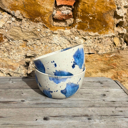 Two ceramic bowls with blue splatter design stacked on a wooden surface against a stone wall.