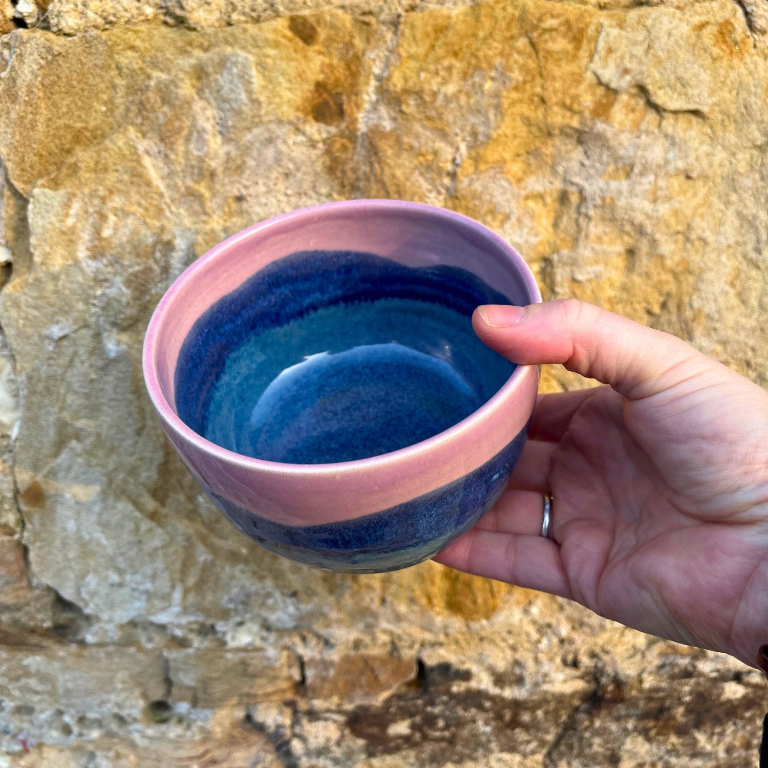 Hand holding a blue ceramic bowl against a stone background