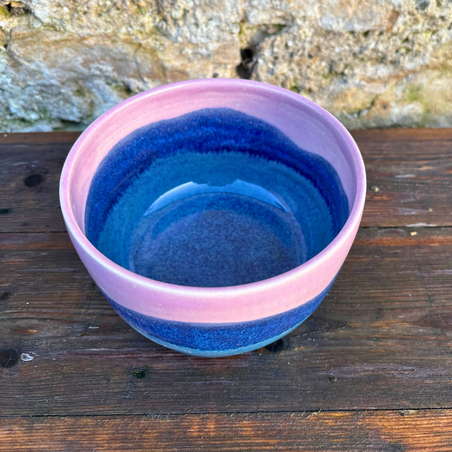 Blue and pink ceramic bowl on a wooden surface with a natural background