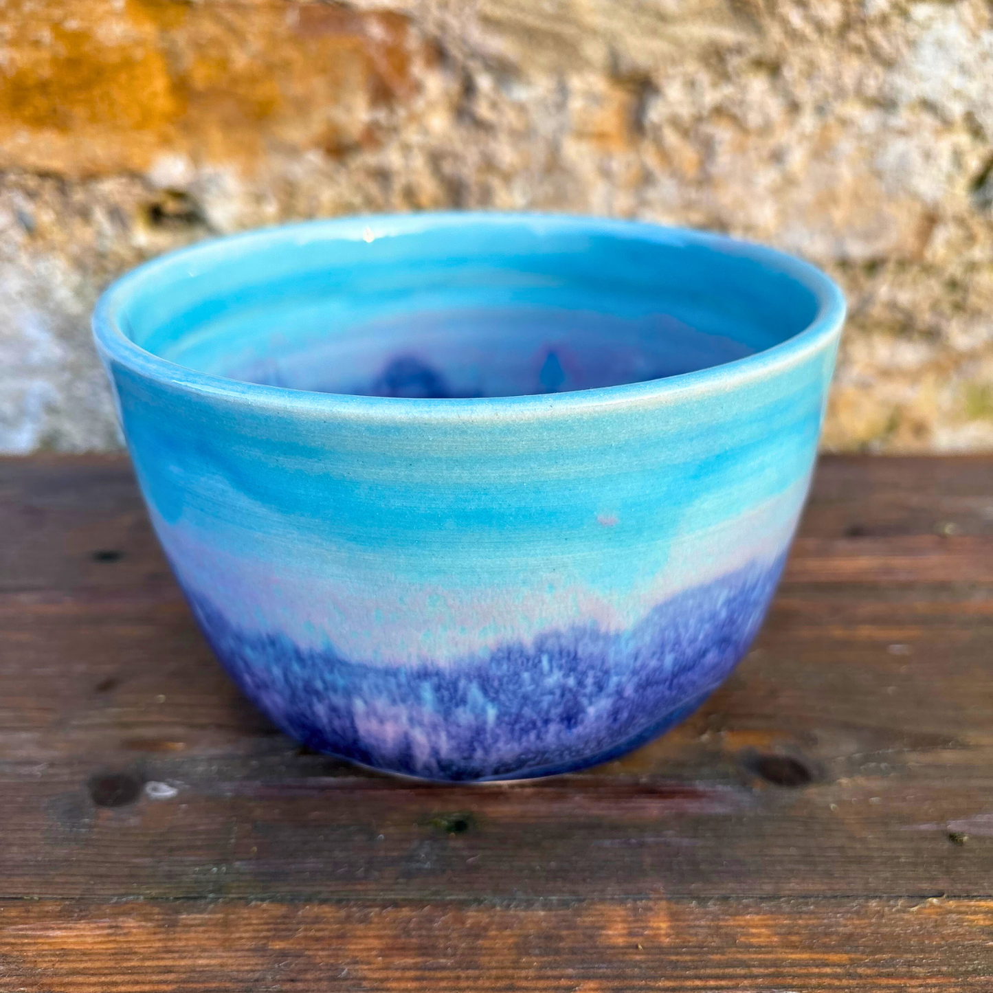 Blue and purple ceramic bowl on a wooden surface with a natural background