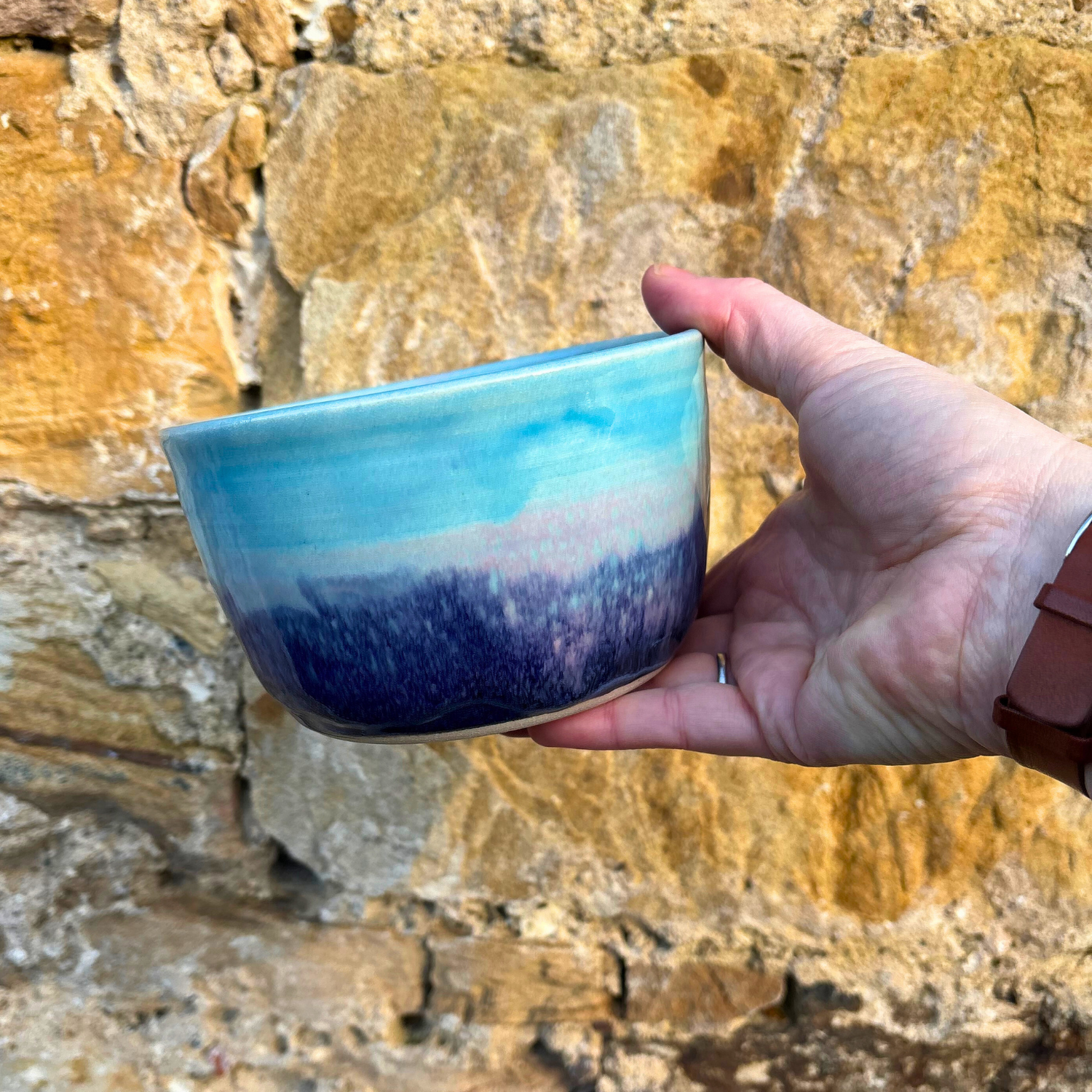 Hand holding a blue ceramic bowl against a stone wall background