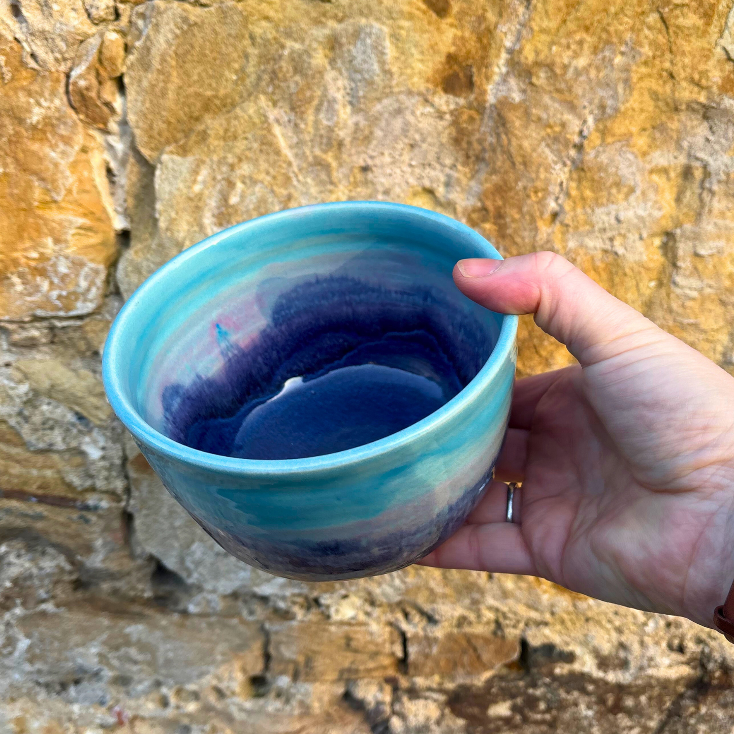 Hand holding a blue ceramic bowl against a stone wall background