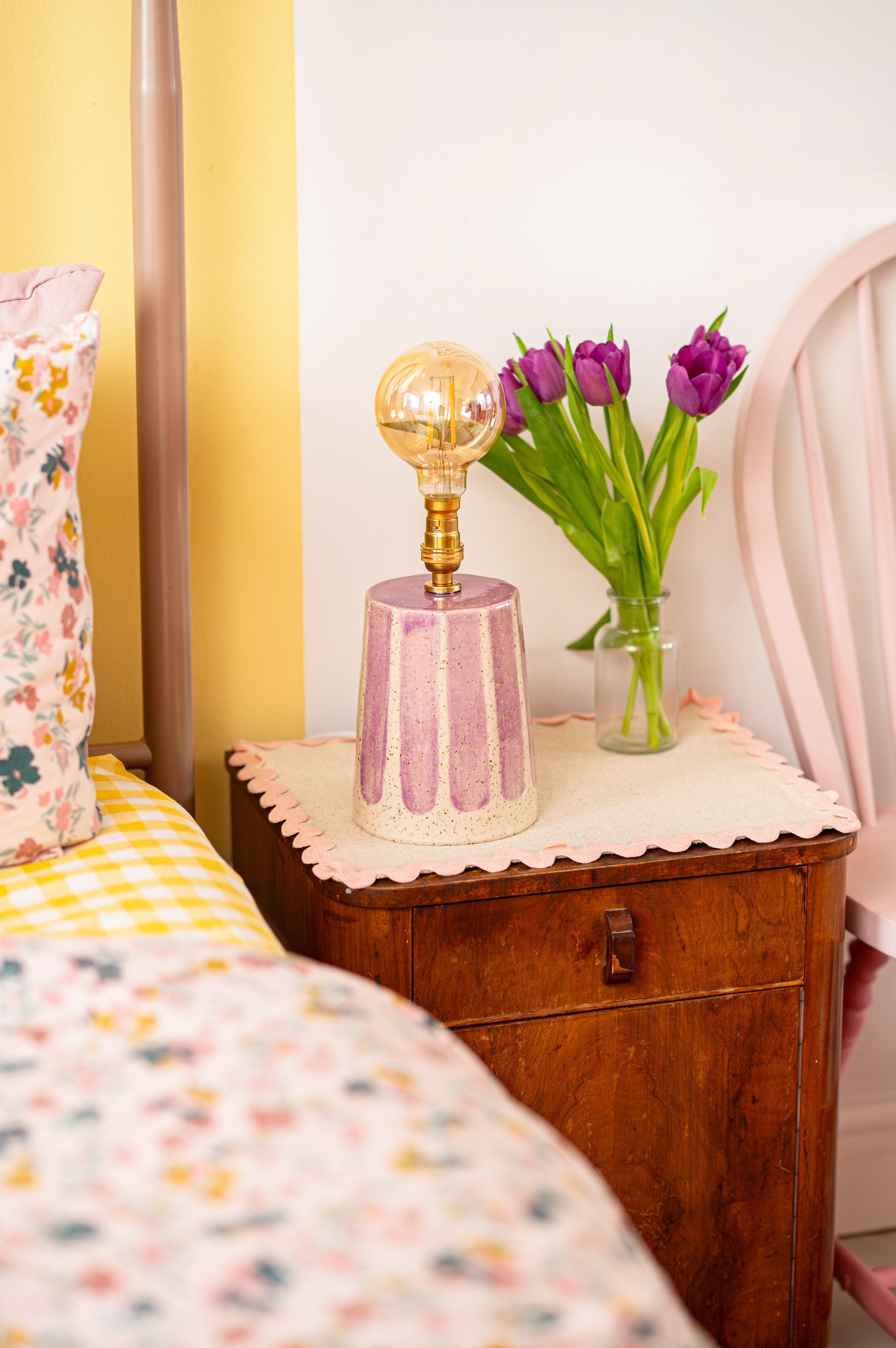 Vintage-style nightstand with decorative lamp and tulips in a bedroom setting