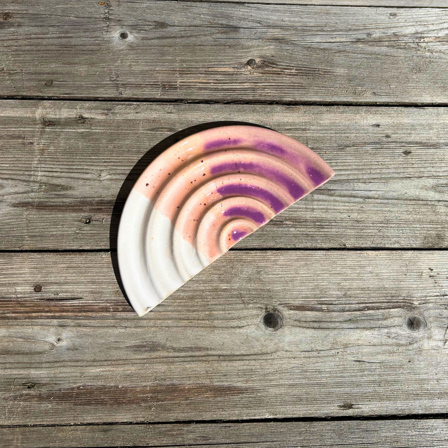 Half-circle ceramic item with concentric color pattern on a wooden surface