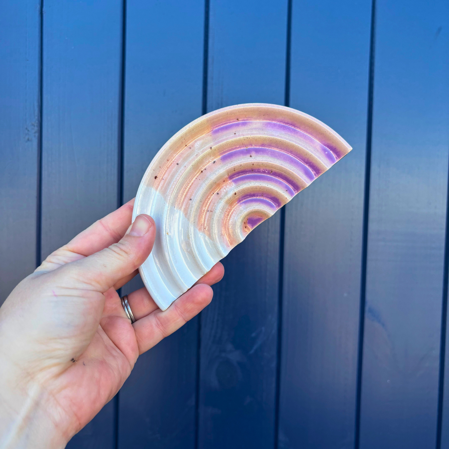 Hand holding a colorful, curved ceramic soap dish against a blue wooden background