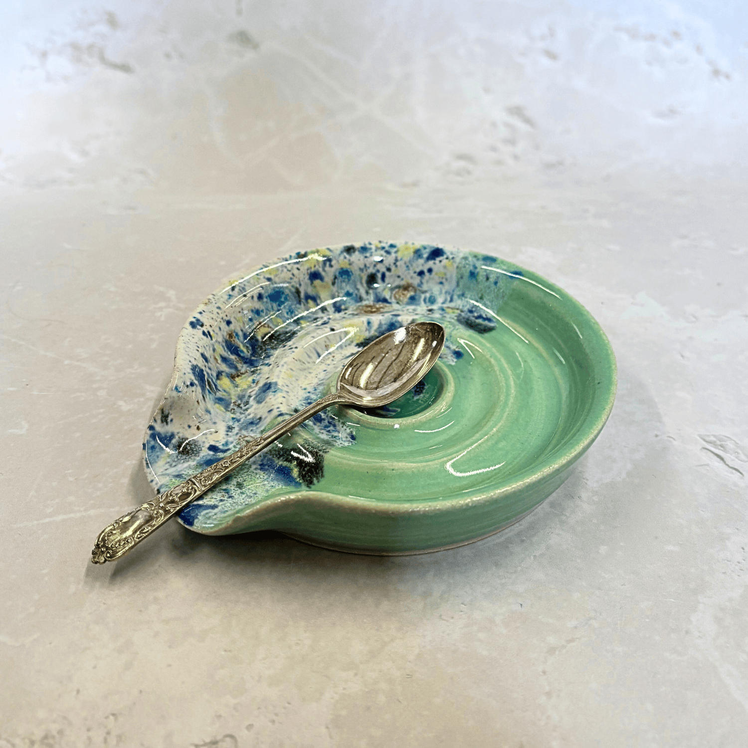 Ella Fletcher Designs Handmade Ceramic Spoon Rest in Green Shoreline, circular spoon rest with ridges, green and multi-coloured speckles with a spoon