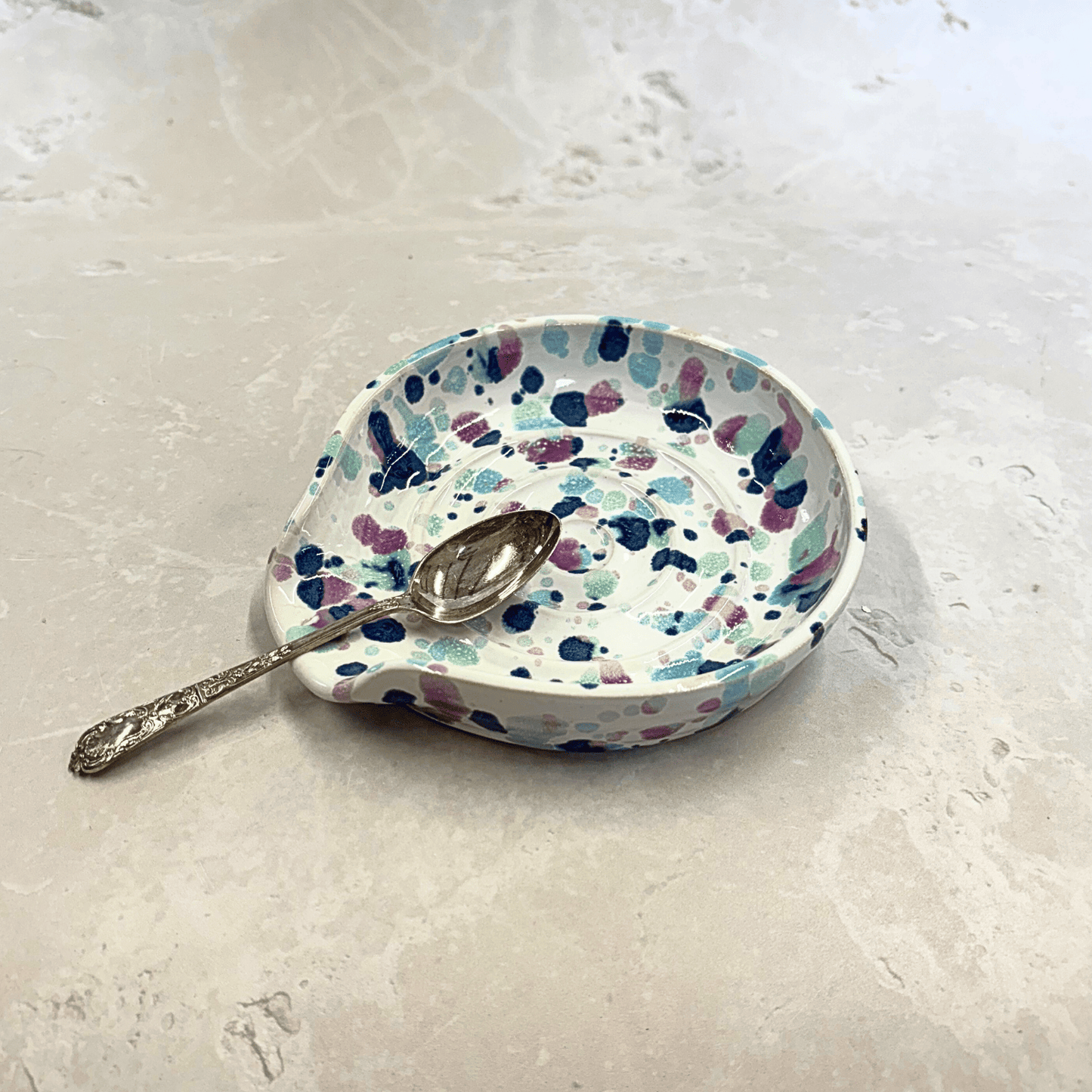 Ella Fletcher Designs Handmade Ceramic Spoon Rest in Sweetpea design, circular spoon rest with ridges, white background with splattered pinks and blues