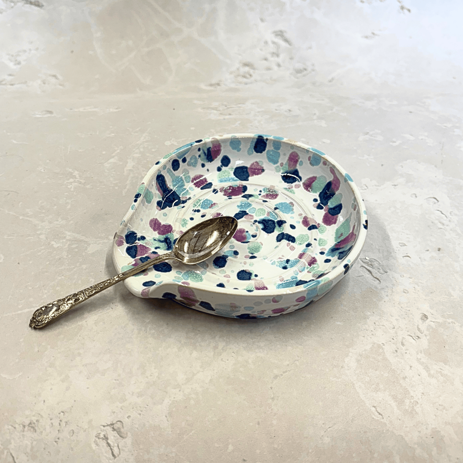 Ella Fletcher Designs Handmade Ceramic Spoon Rest in Sweetpea design, circular spoon rest with ridges, white background with splattered pinks and blues