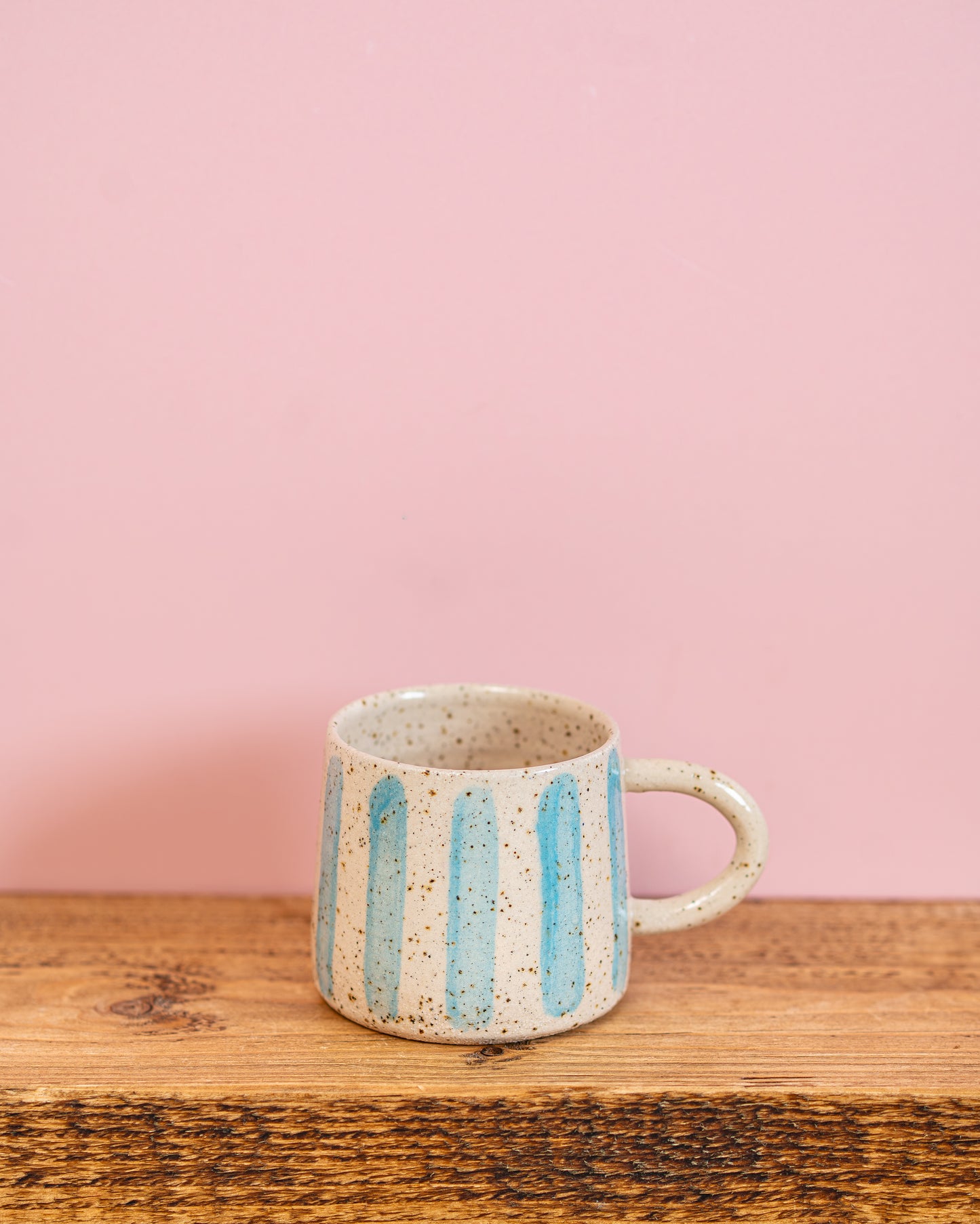 Ceramic mug with blue stripes on a wooden surface and pink background