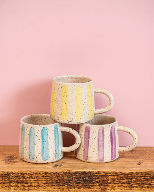 Three ceramic mugs with striped patterns on a wooden surface and pink background