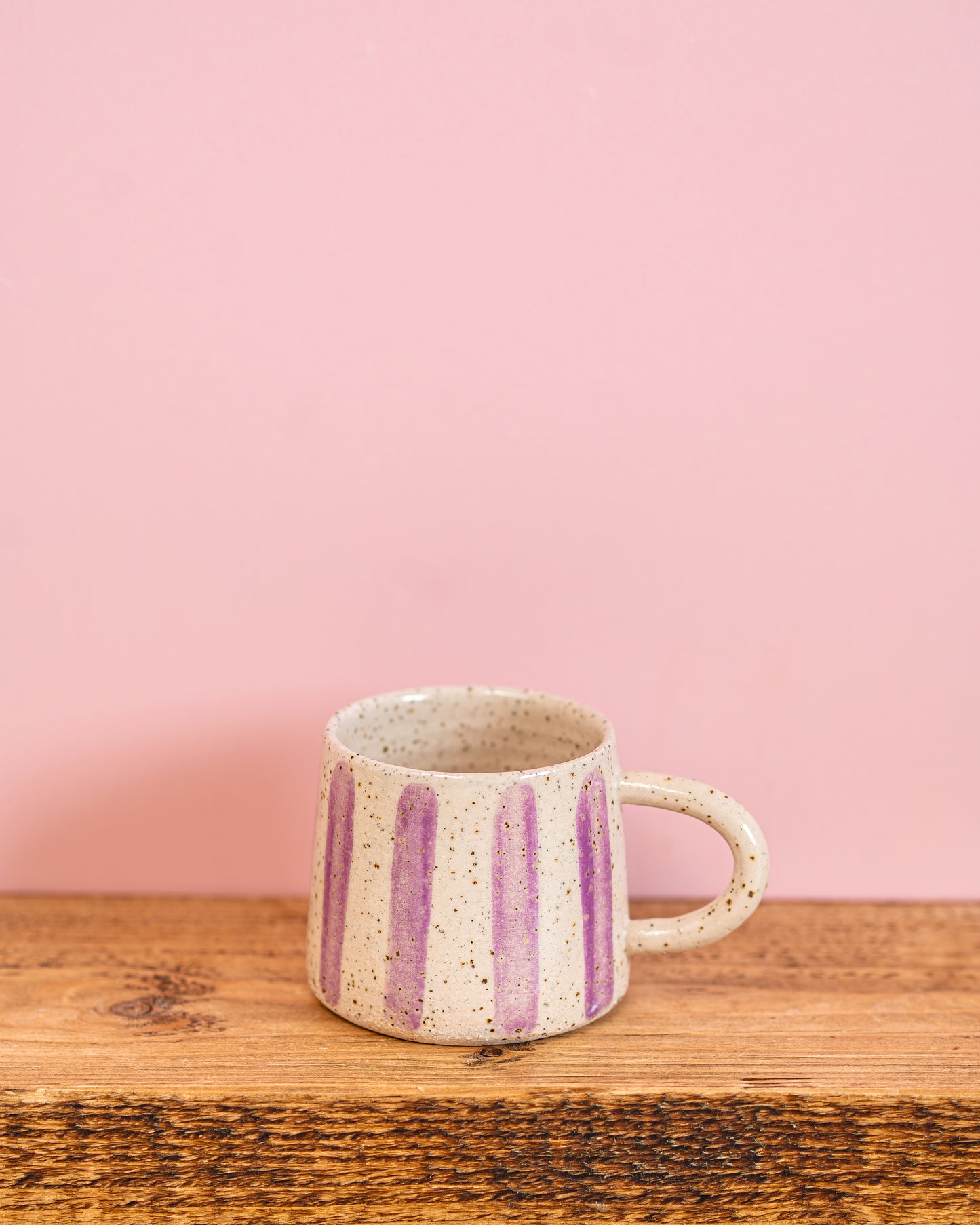 Ceramic mug with purple stripes on a wooden surface and pink background