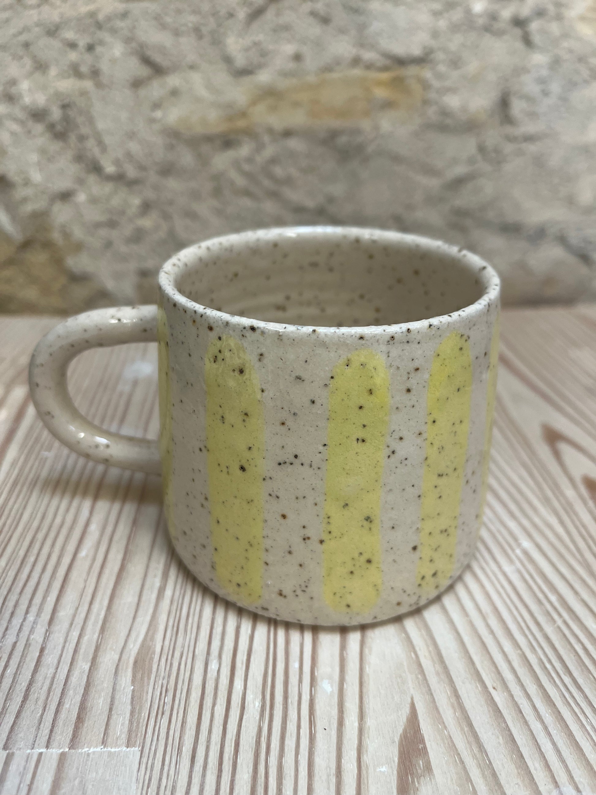 Speckled ceramic mug with yellow stripes on a wooden surface