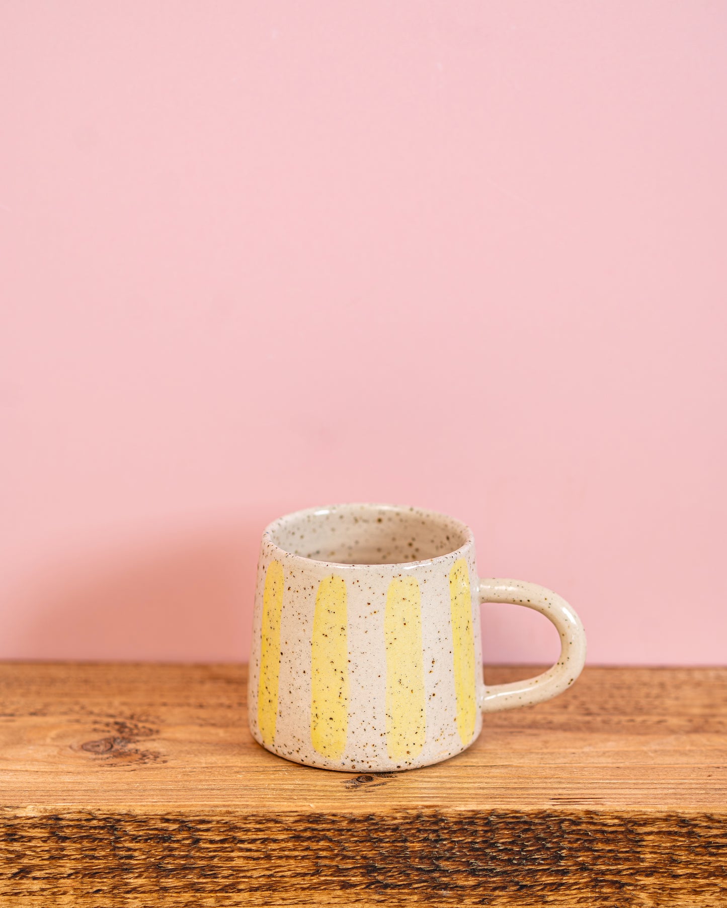 Ceramic mug with yellow stripes on a wooden surface and pink background