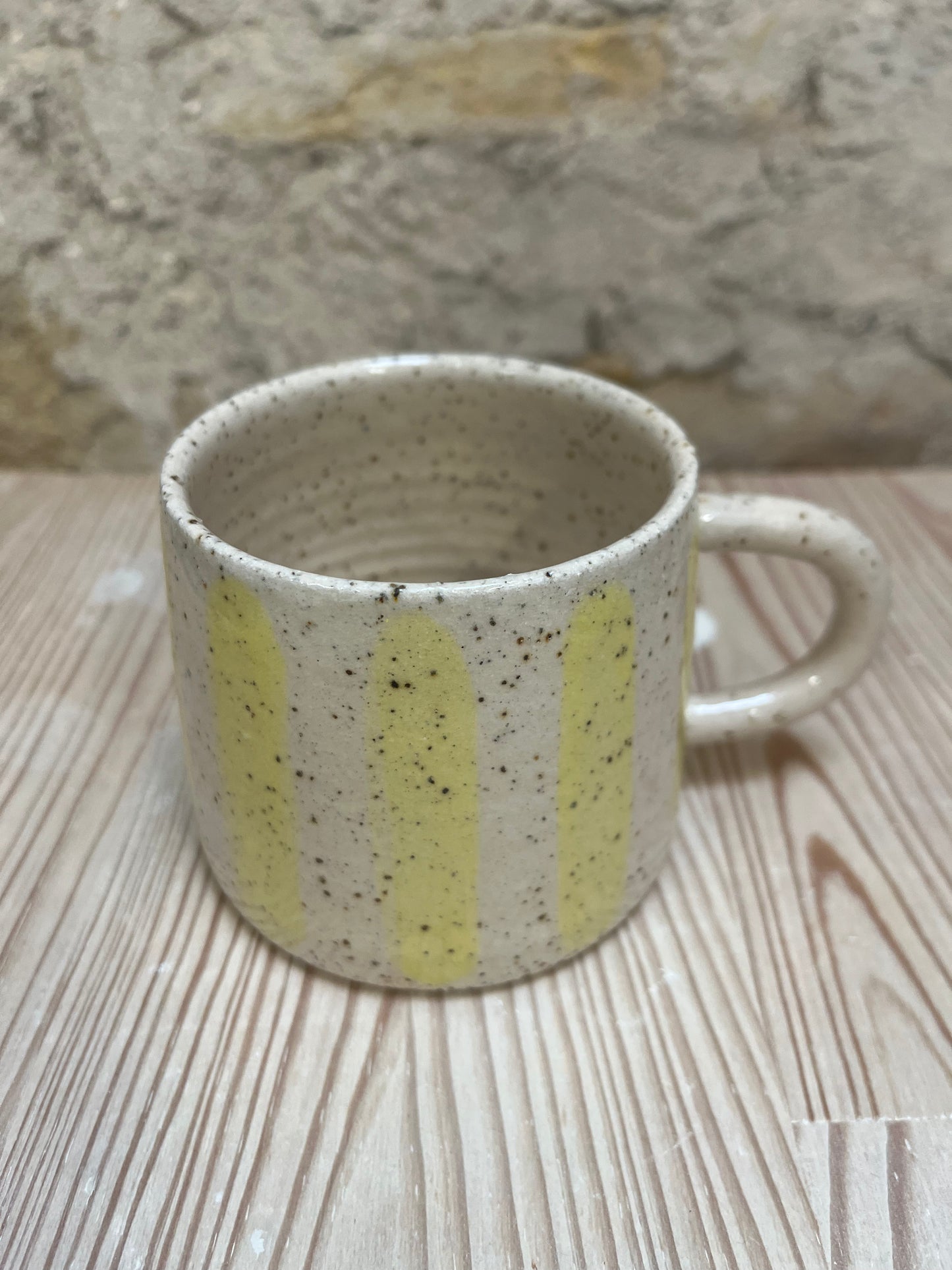Speckled ceramic mug with yellow stripes on a wooden surface.