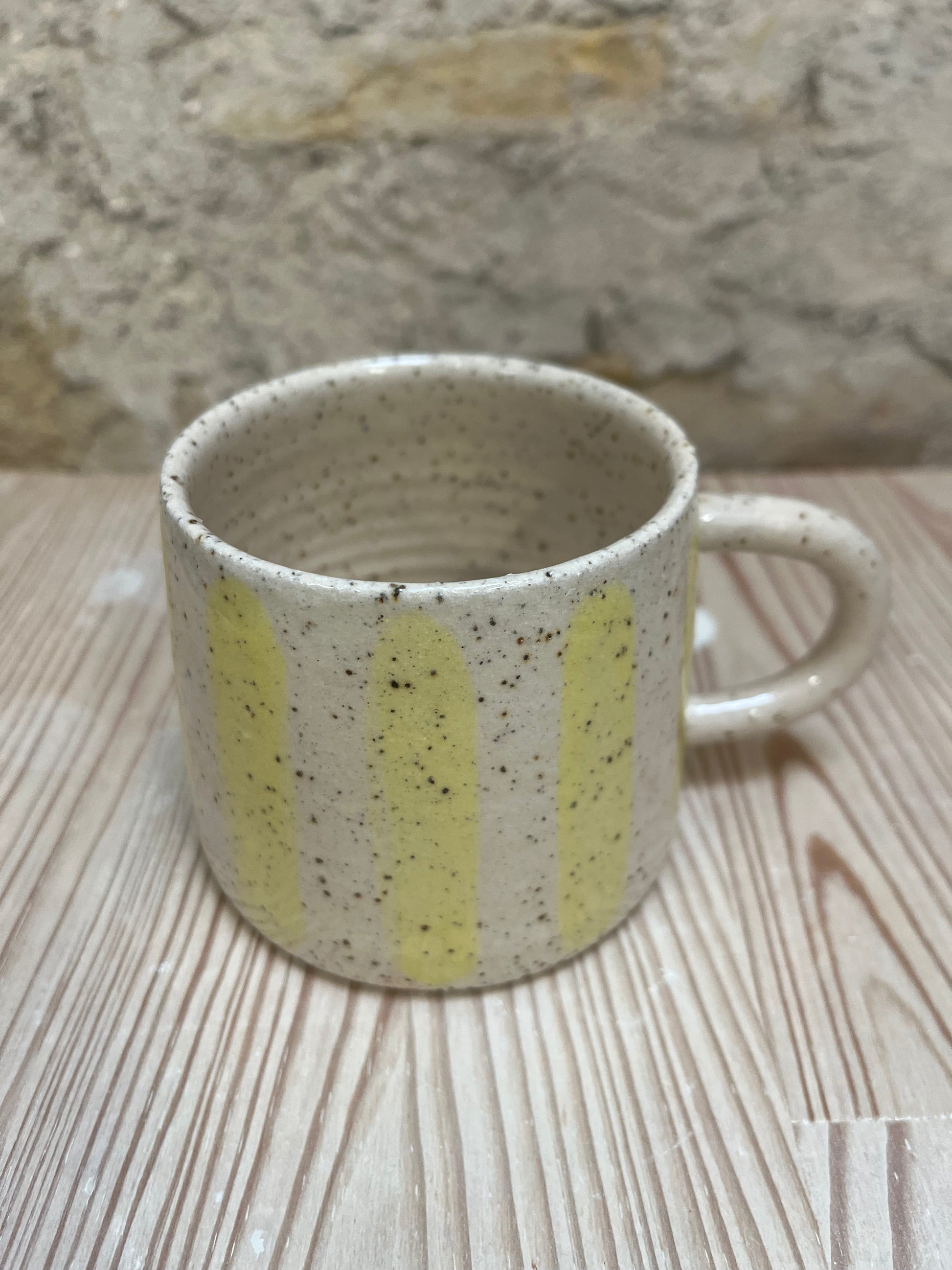 Speckled ceramic mug with yellow stripes on a wooden surface.