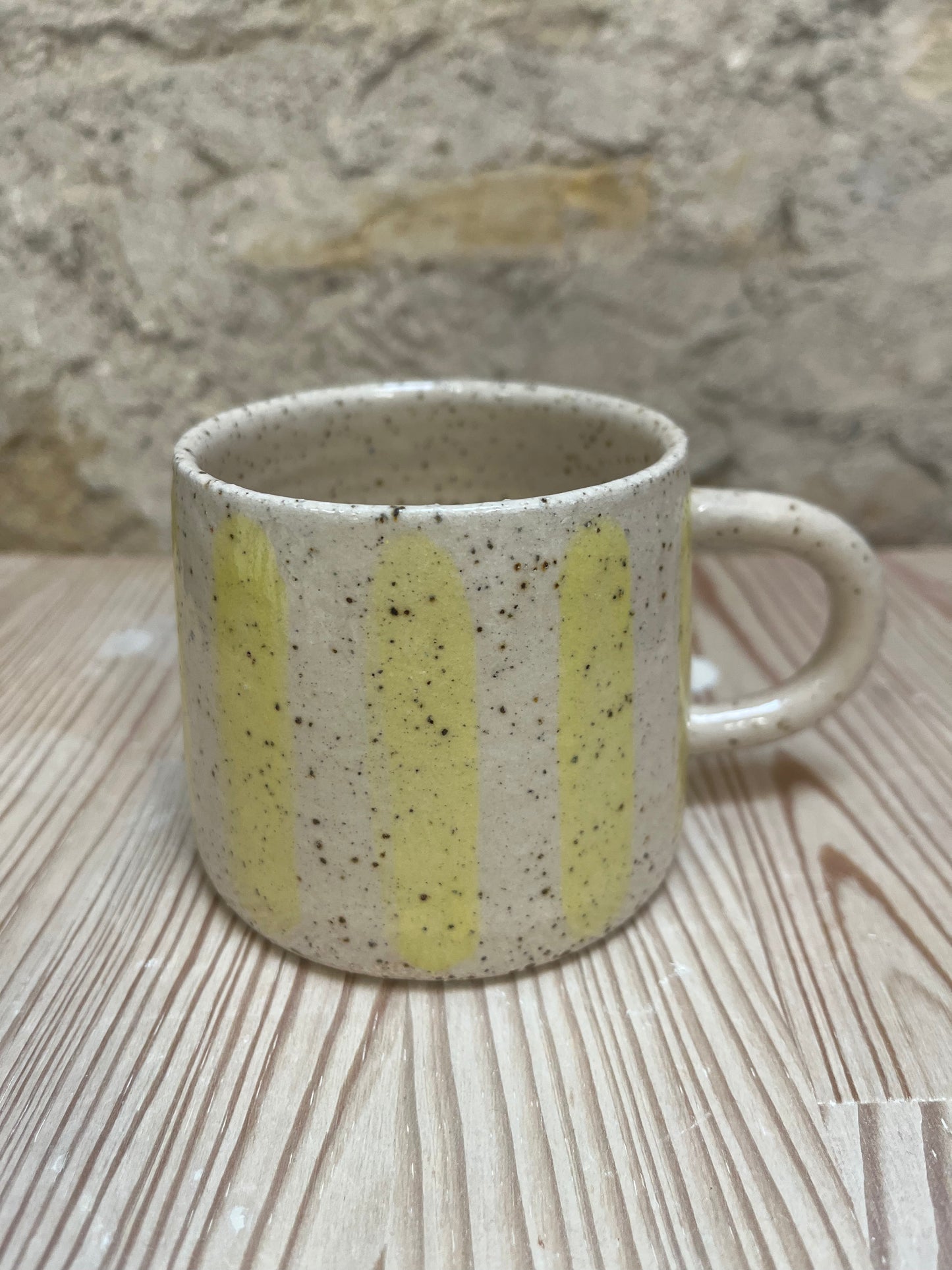 Speckled ceramic mug with yellow stripes on a wooden surface.