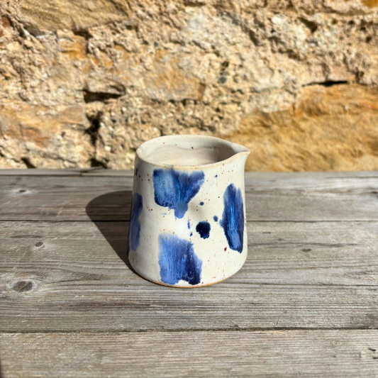 Ceramic cup with blue splotches on a wooden surface with a rocky background