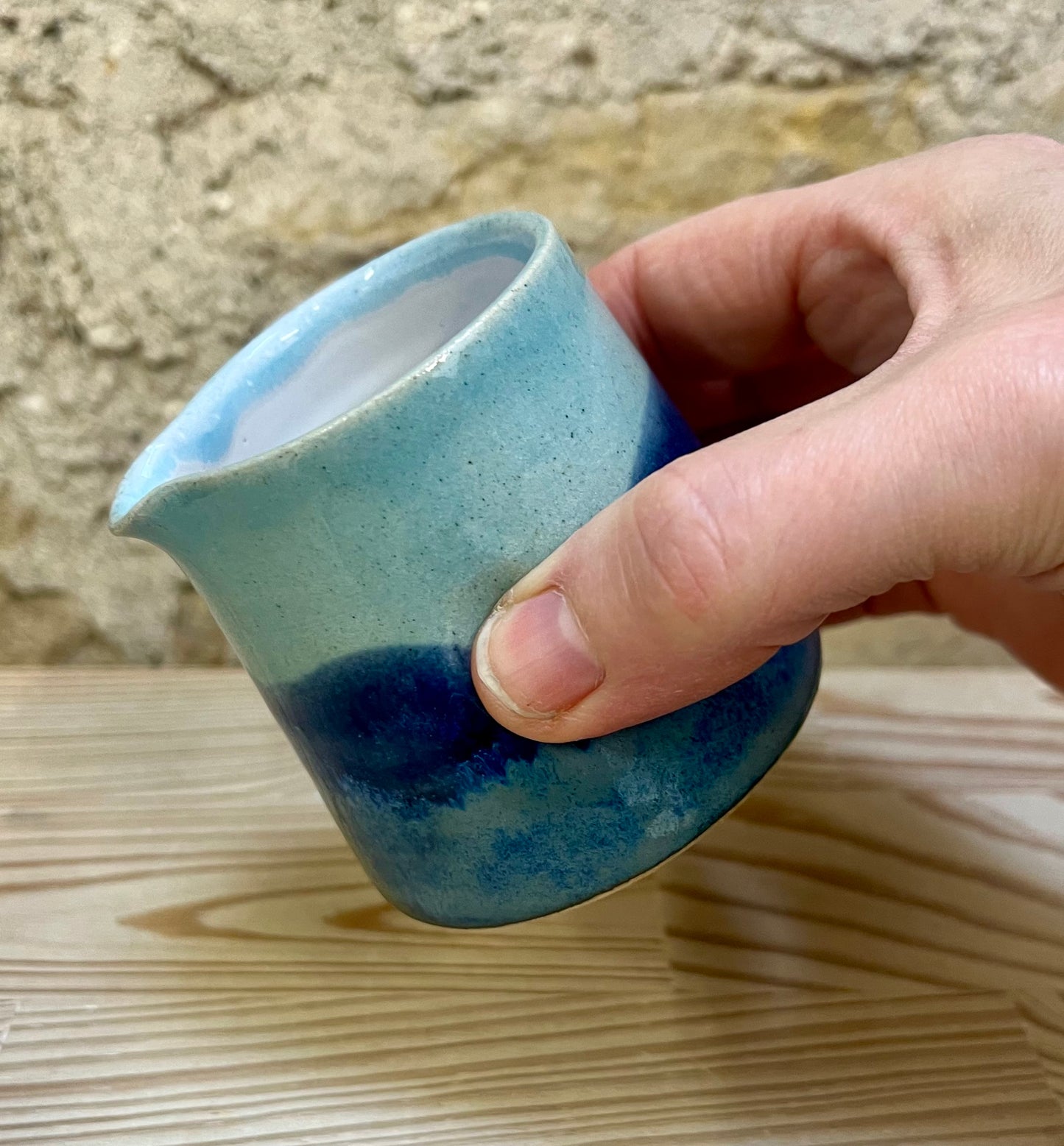 Hand holding a blue ceramic cup against a stone wall background