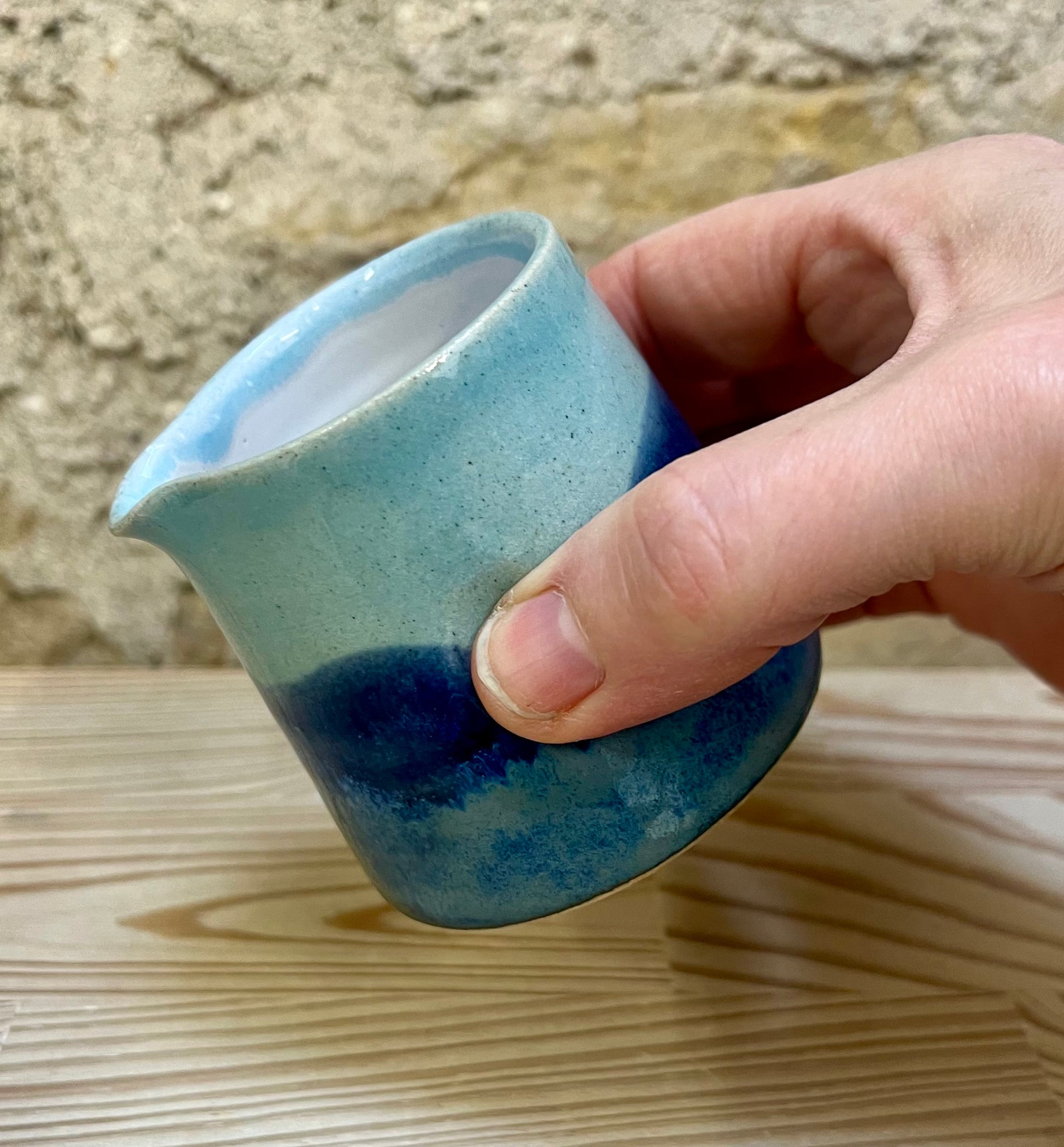 Hand holding a blue ceramic cup against a stone wall background