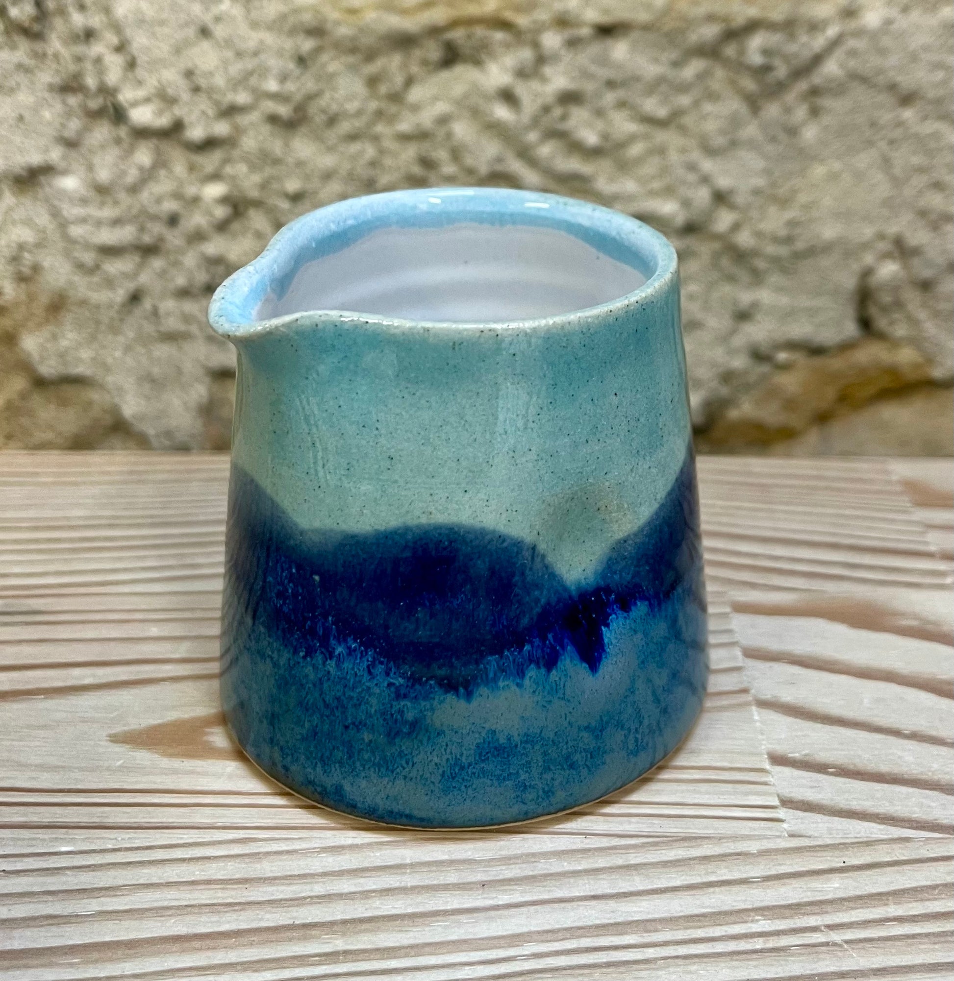 Blue ceramic pitcher on a textured surface with a stone wall background