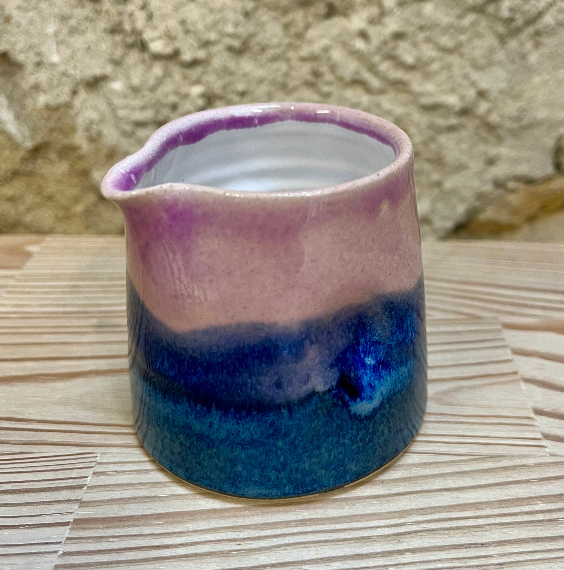 Ceramic pitcher with pink and blue gradient on a woven surface