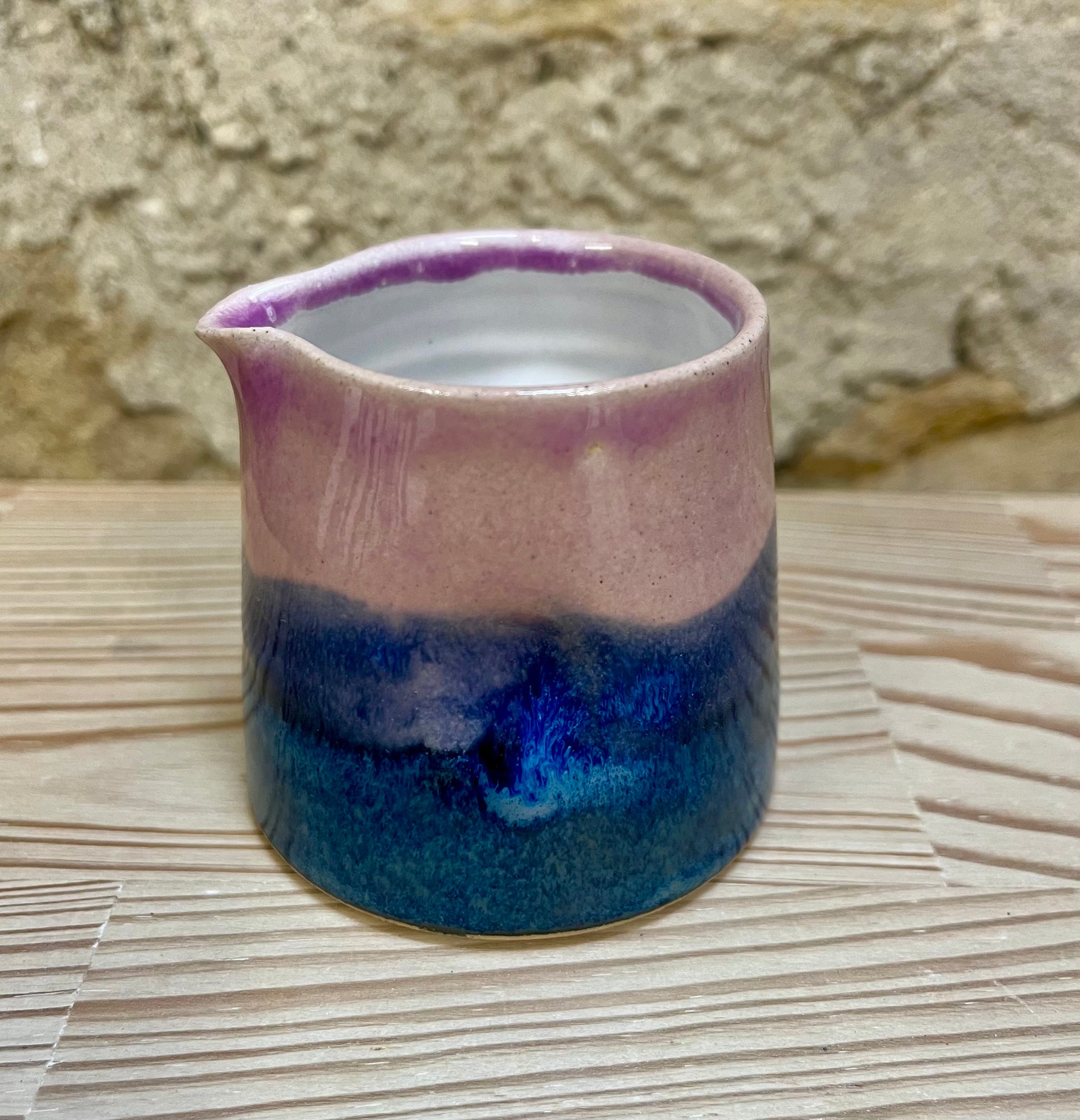 Ceramic pitcher with pink and blue gradient on a stone surface
