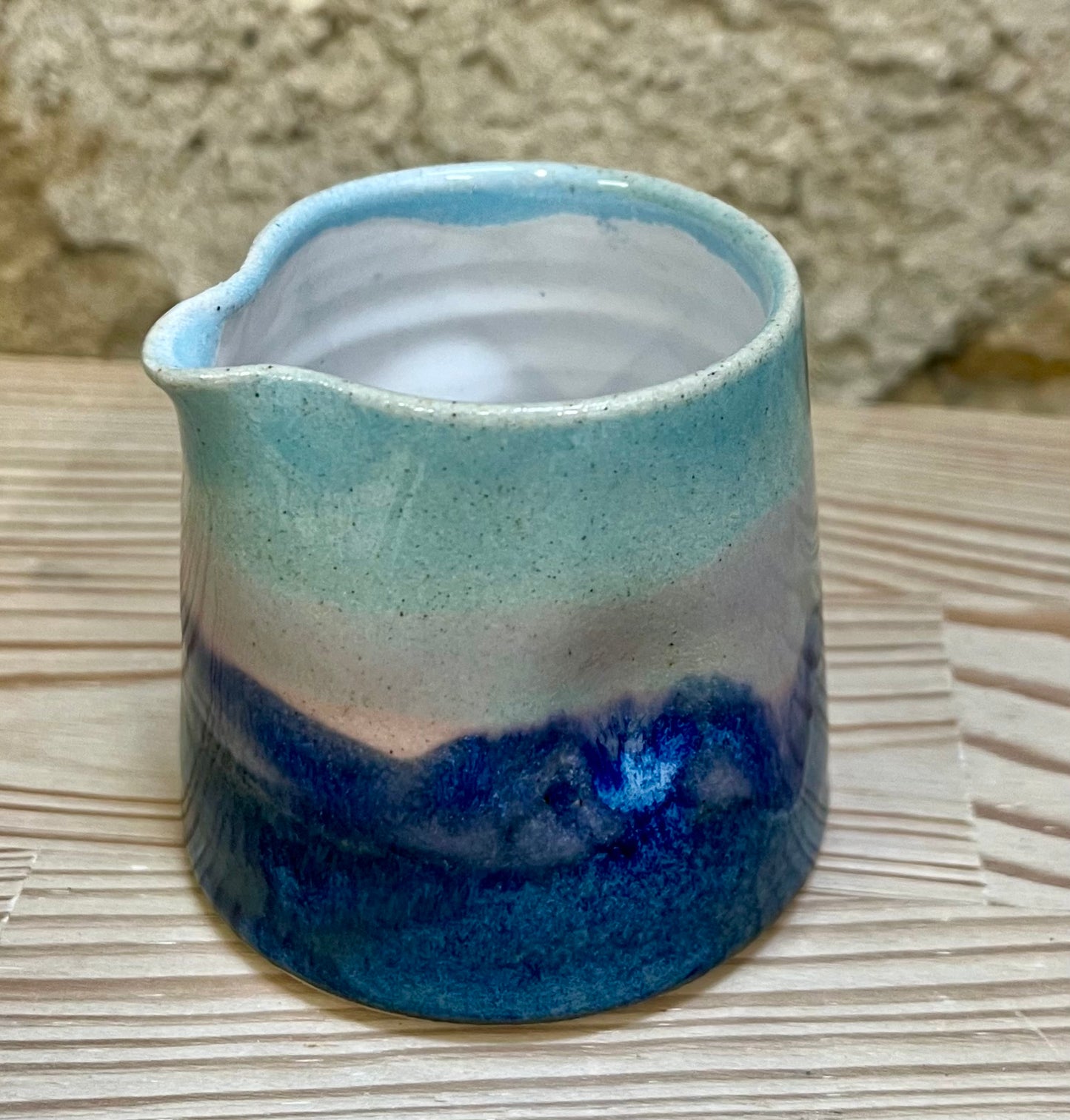 Ceramic pitcher with blue and pink gradient on a textured surface