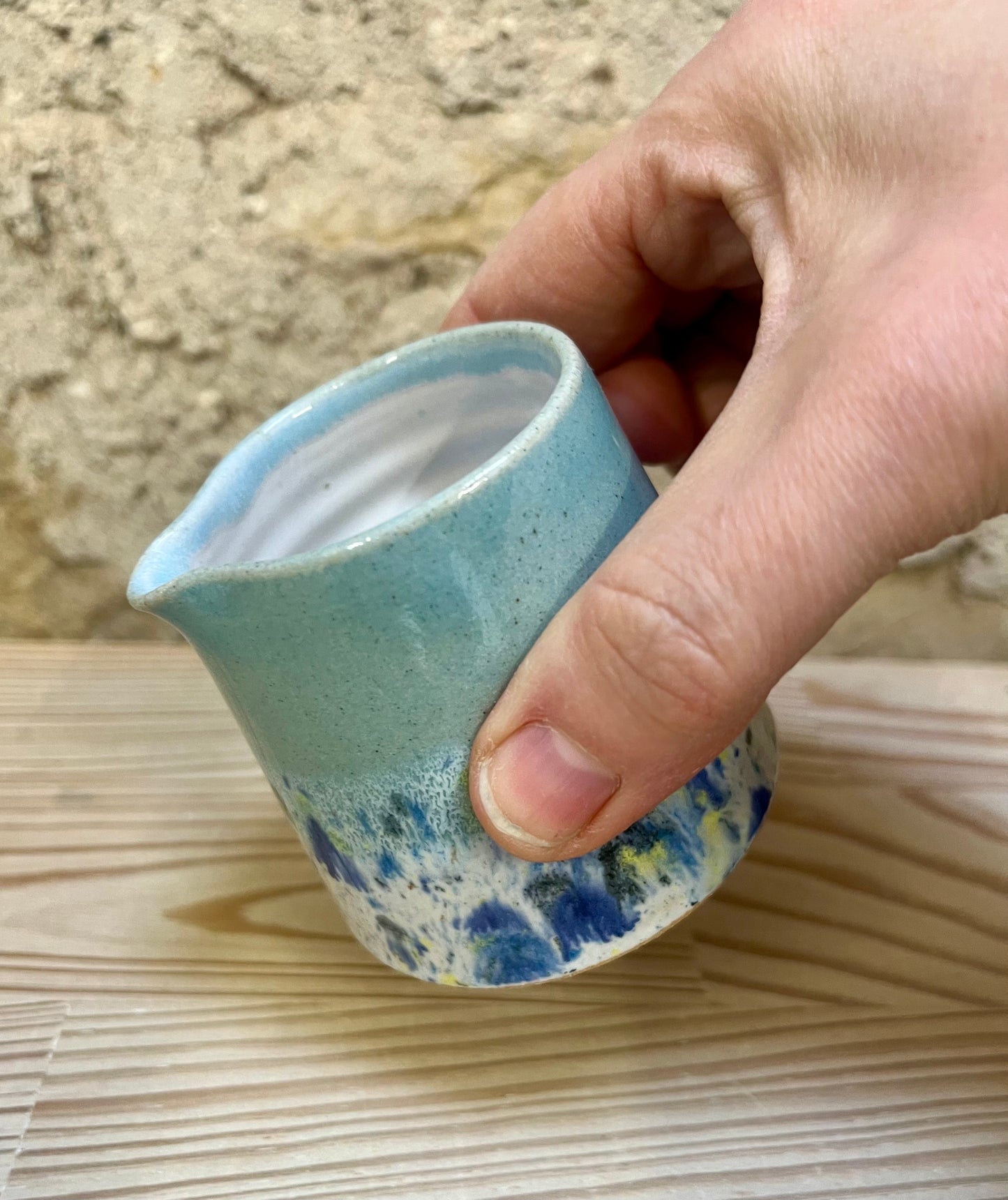 Hand holding a small ceramic jug with blue and white speckled design on a wooden surface.
