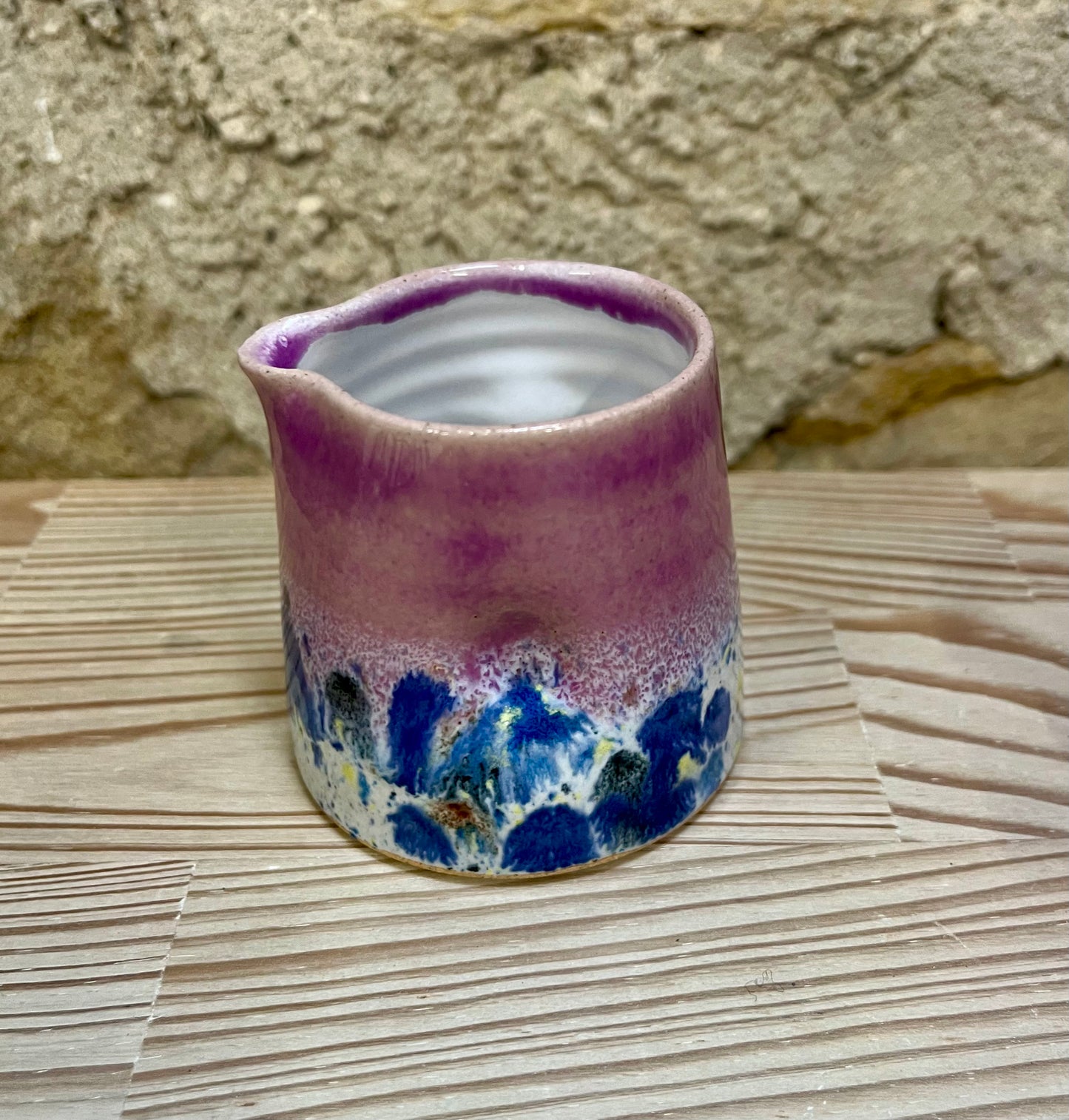 Ceramic pitcher with pink and blue glaze on a woven surface