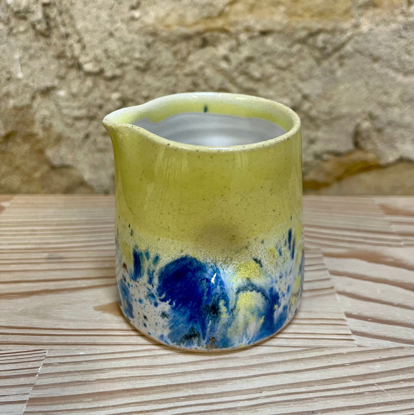 Ceramic pitcher with a yellow body and blue and white speckled pattern on a stone surface.