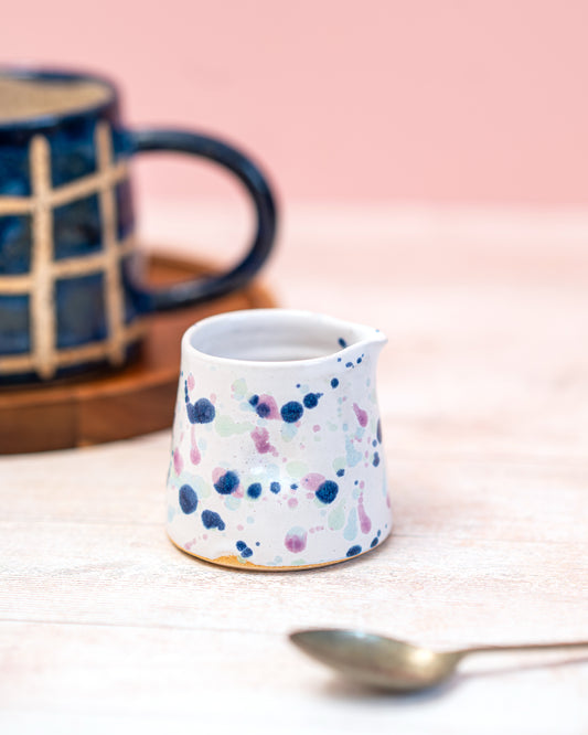 Small ceramic pitcher with colorful speckled design on a light pink background